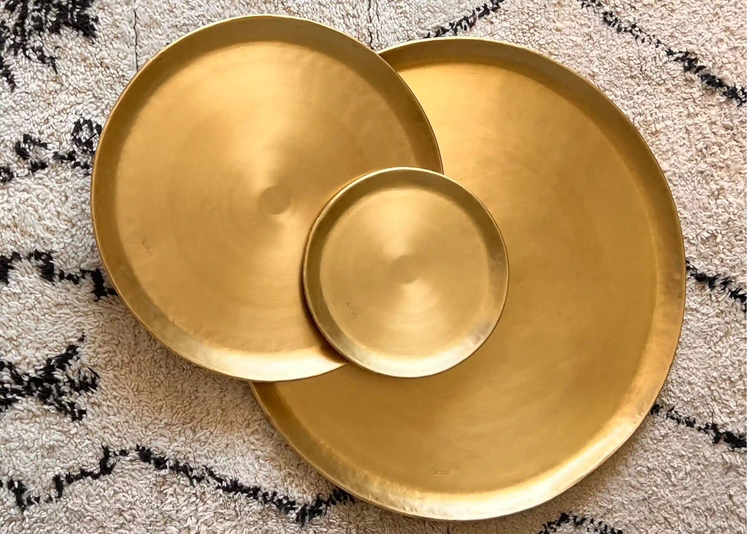 Ensemble déco en laiton doré, coussin blanc et noir aux motifs floraux, et tapis en toile de fond, photo prise de haut