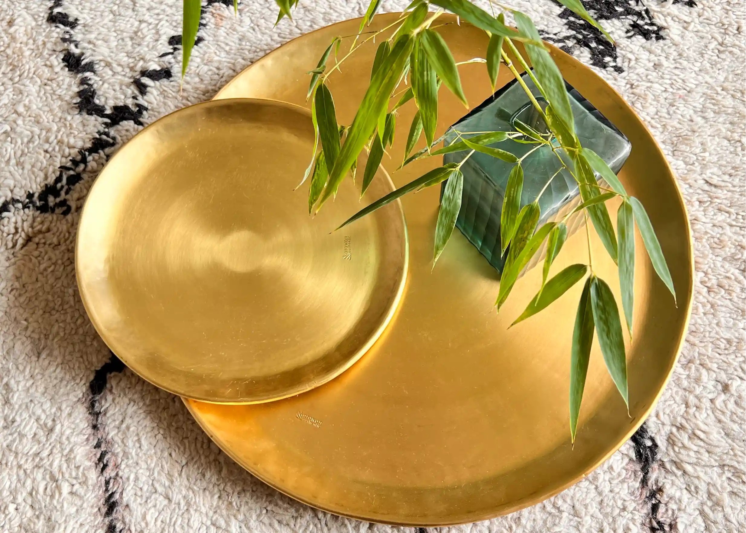 Coupelles et plateaux en laiton lisse doré empilés, de différentes tailles, une branche de fougère verte visible