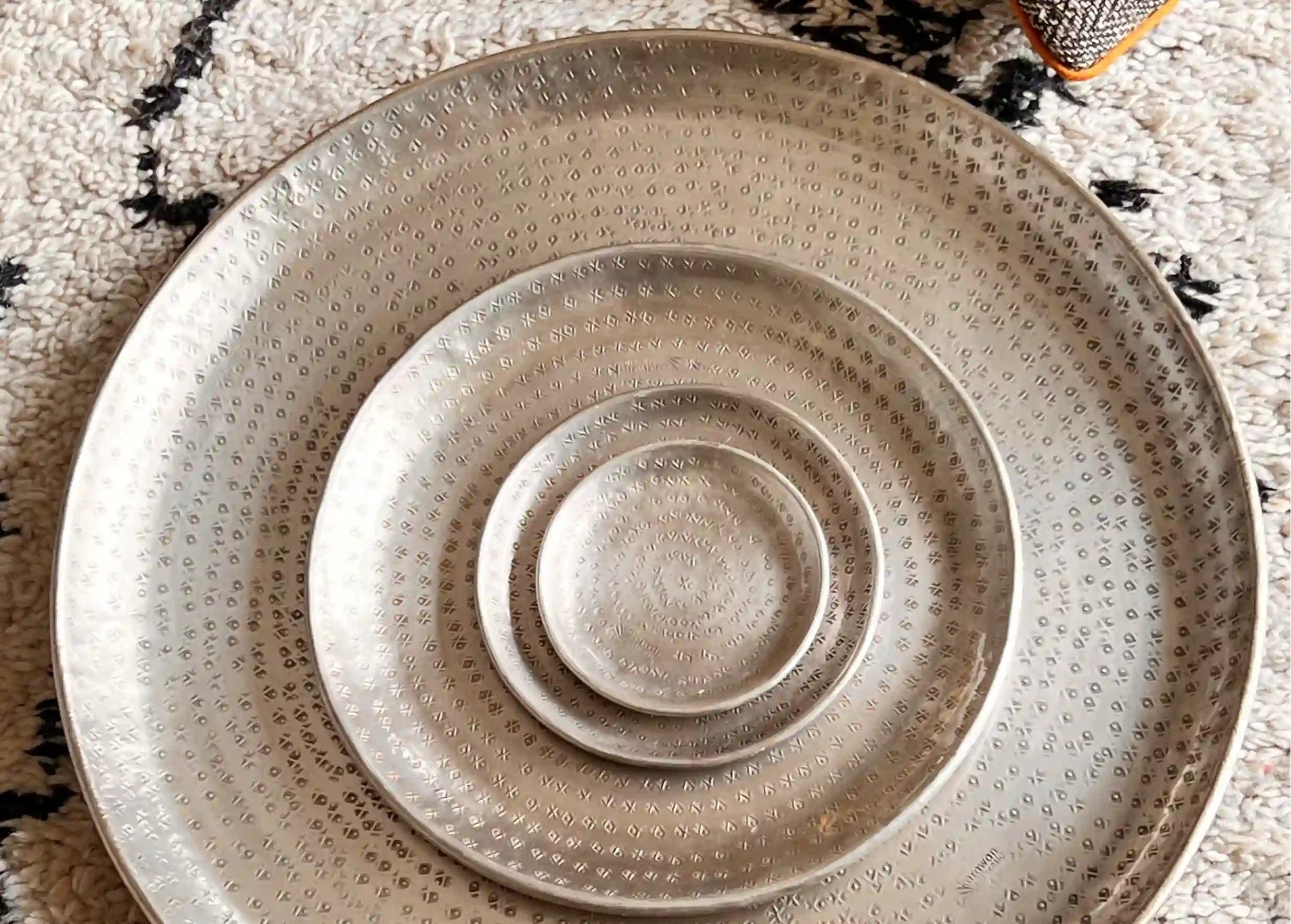 Plateaux en laiton argenté martelé et gravé, de tailles décroissantes, posés sur un tapis à motifs noirs et blancs