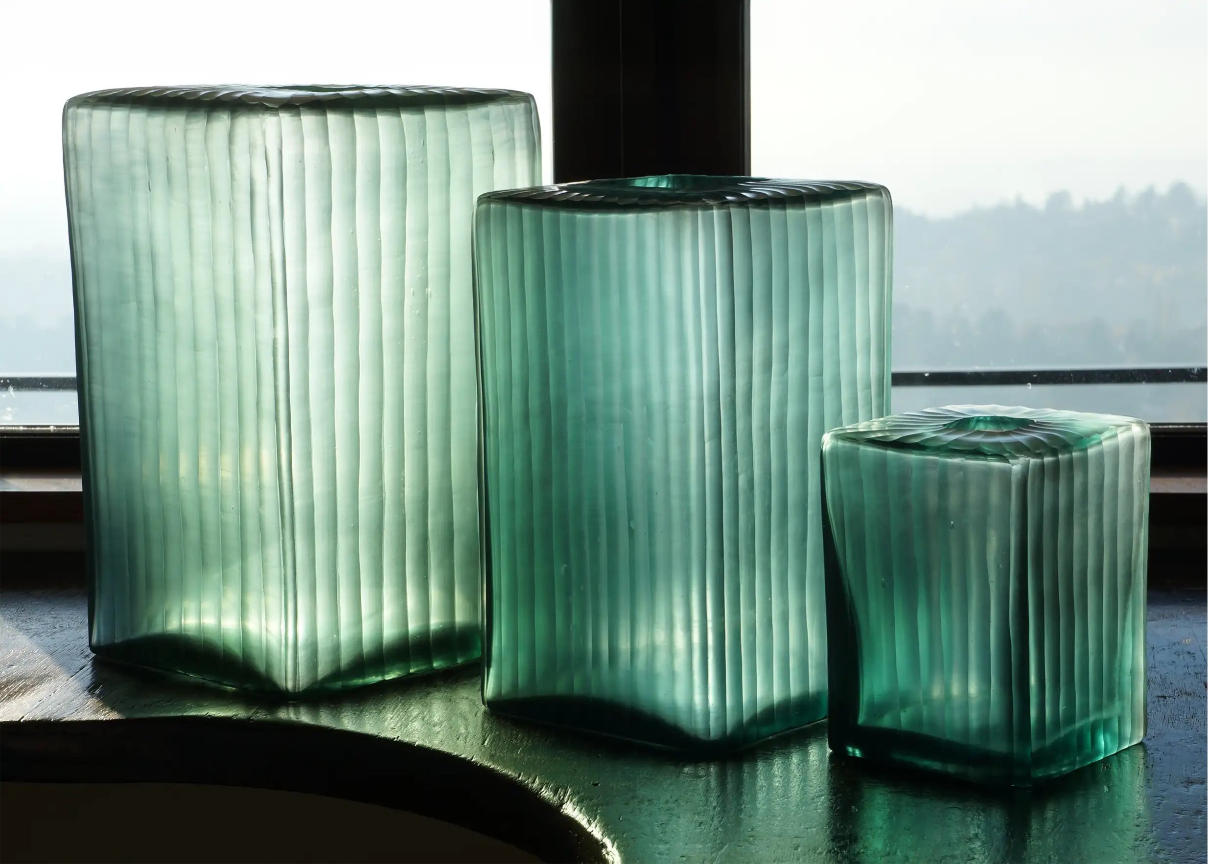 Trio de vases aqua cube, en verre soufflé et recyclé, posés du plus petit au plus grand devant une fenêtre
