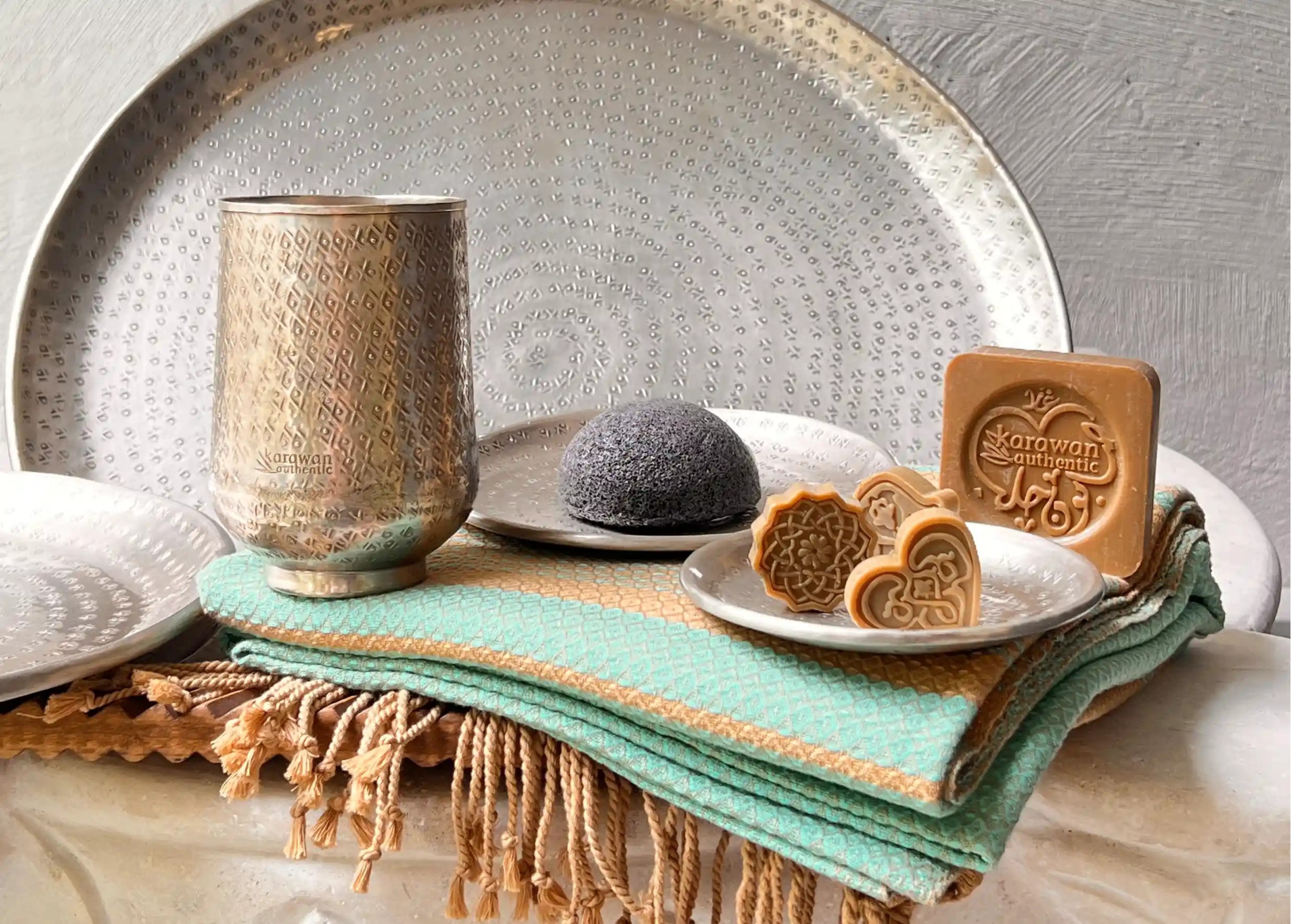 Close-up of the silver-plated brass Palmyr glass and its engravings, with an organic cotton fouta underneath and a natural soap