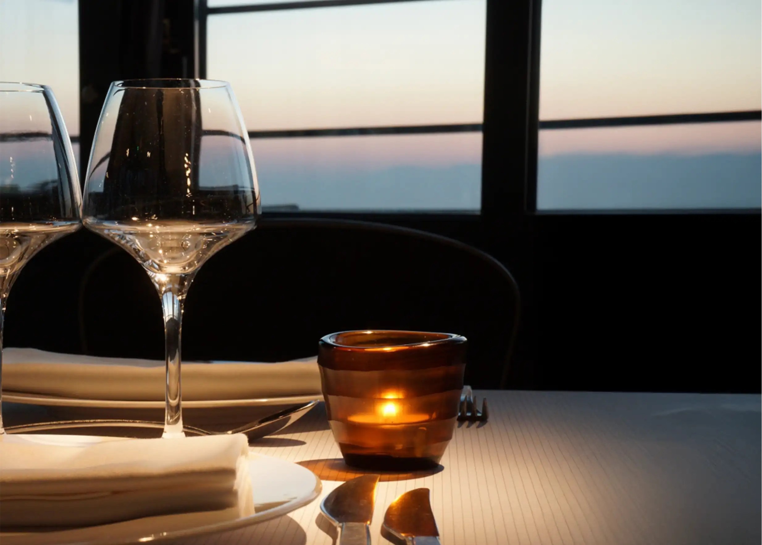 Amber-colored blown glass tea light holder on a dining table, window in the background, evening atmosphere