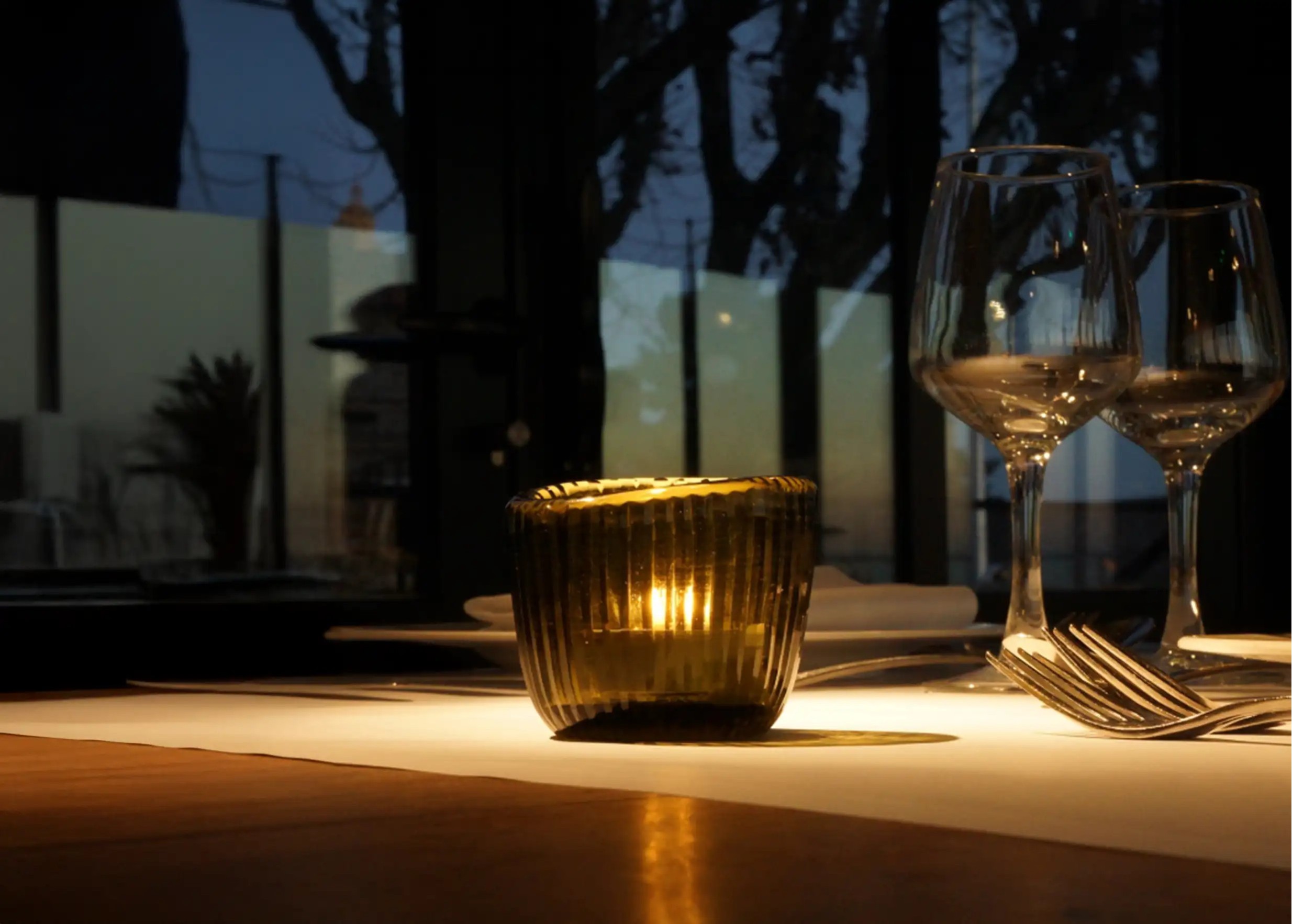Cactus-colored blown glass tea light holder illuminating a table set with glasses and cutlery, in a subdued atmosphere