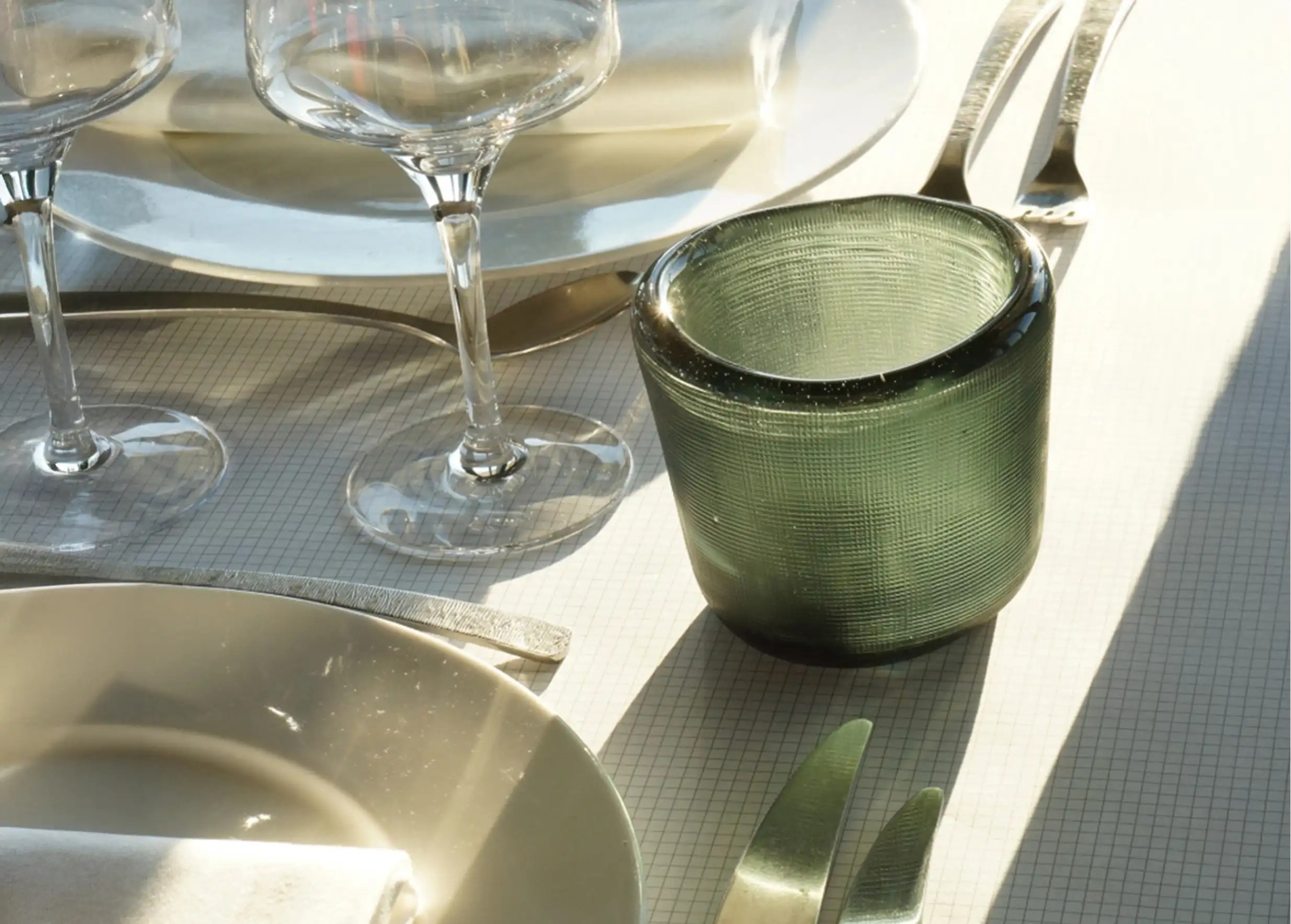 Sage-colored, blown and recycled glass tealight holder on a table set with glasses and cutlery