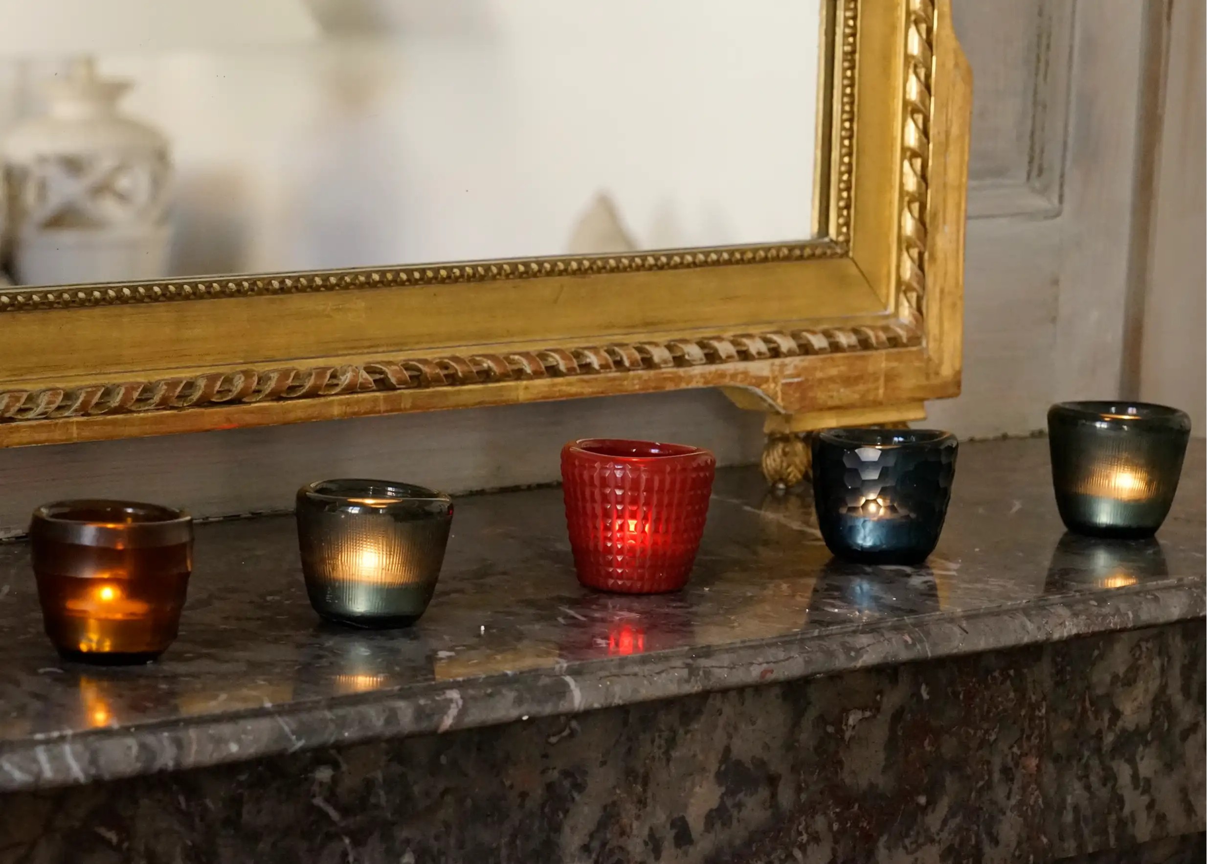 Collection of Karawan glass tealight holders, perfectly aligned on a ledge in front of a mirror