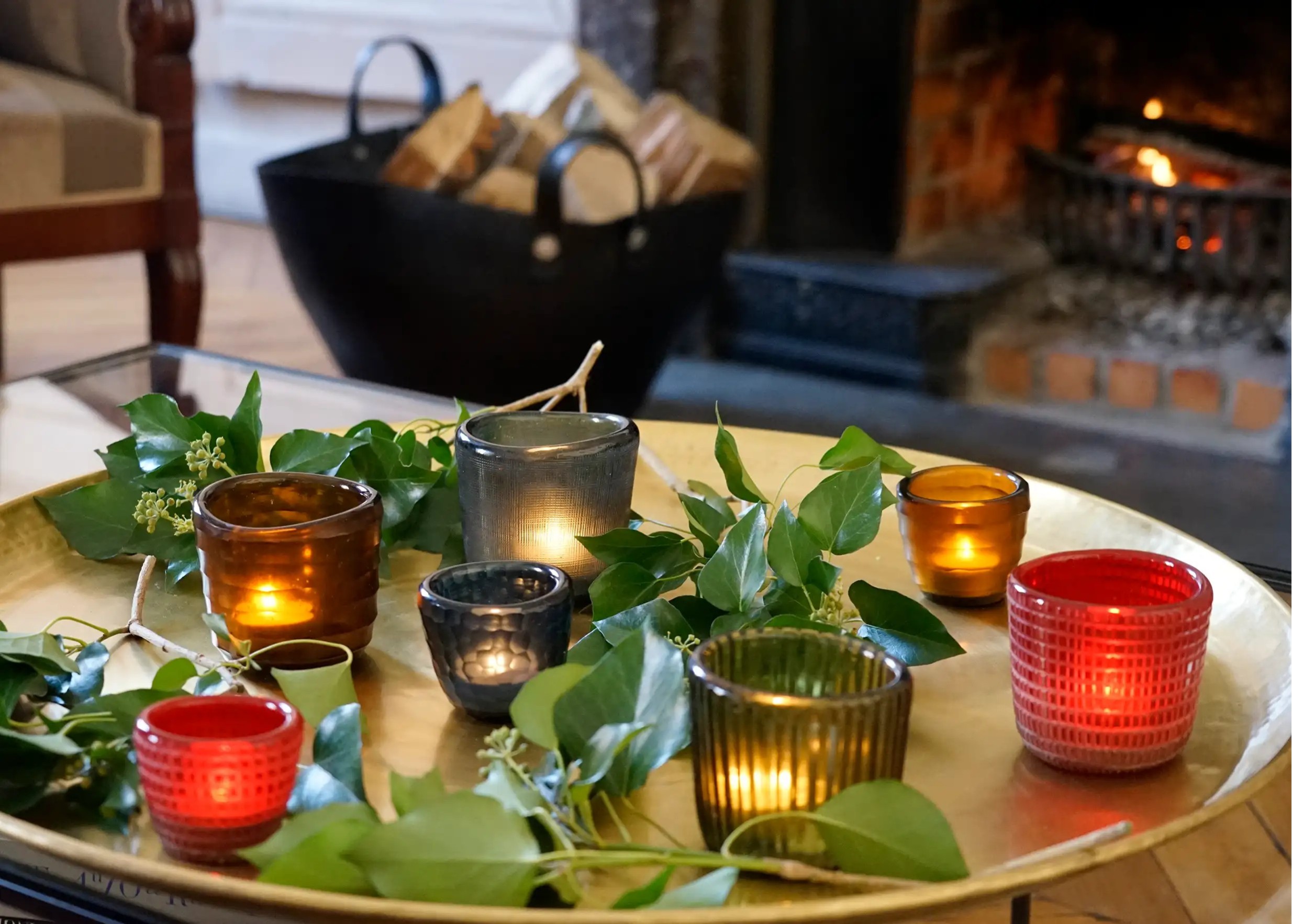 A set of blown glass tealight holders in different colors arranged in a living room near a lit fireplace