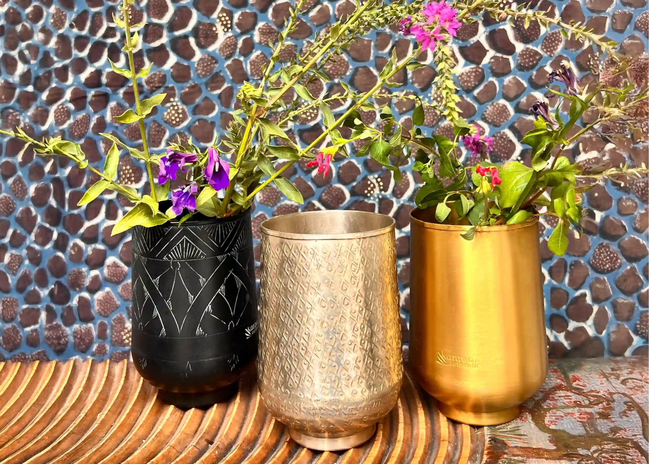Trio de verres gravés en laiton, un verre noir, un verre doré, un verre argenté, des compositions florales colorées