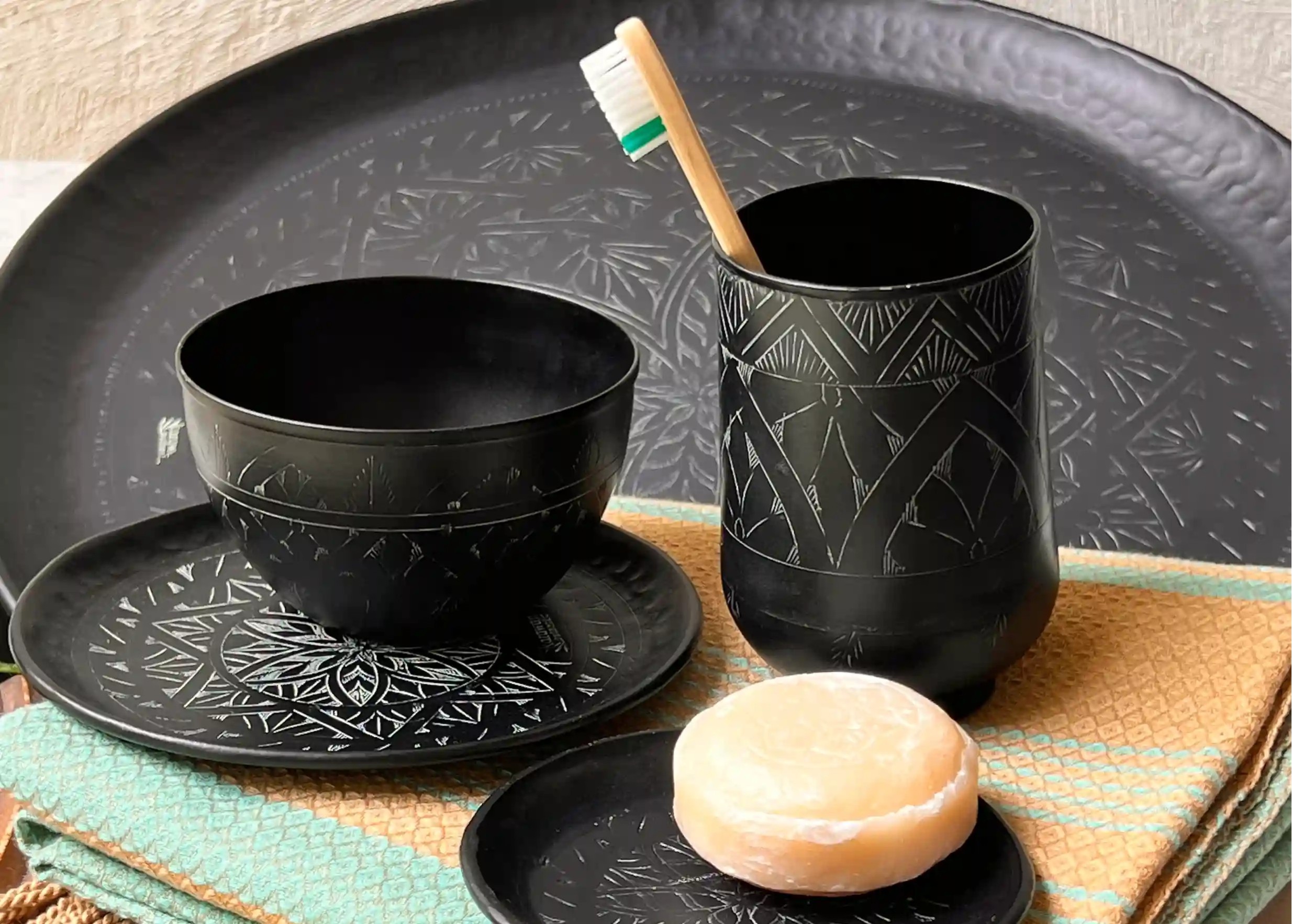 Verre, bol et coupelle en laiton noir avec des motifs gravés posé sur une fouta en coton bio, accompagné d'un savon rond