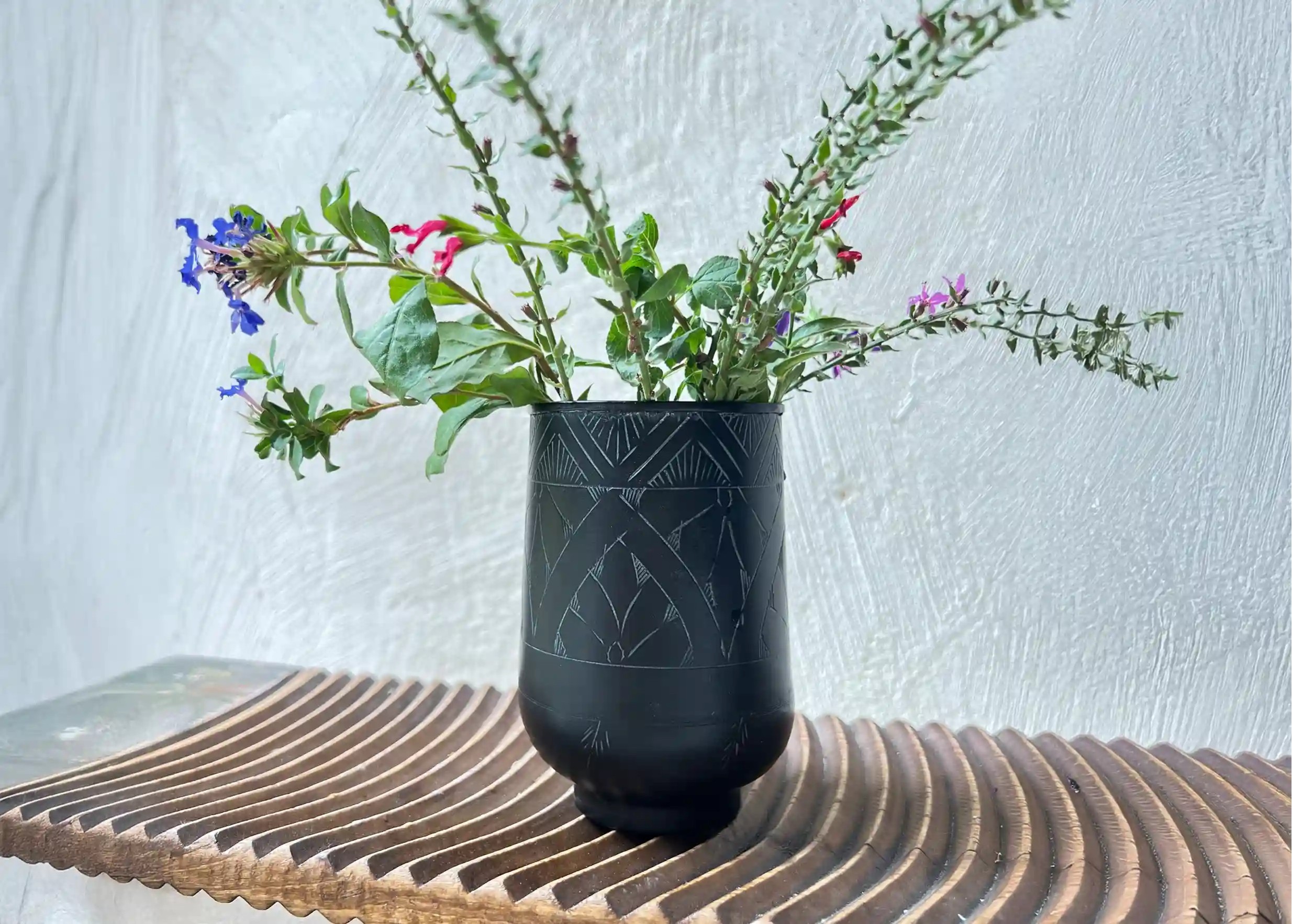 Verre noir gravé en laiton, un bouquet de fleurs colorées et des feuillages verts, posé sur une surface en bois