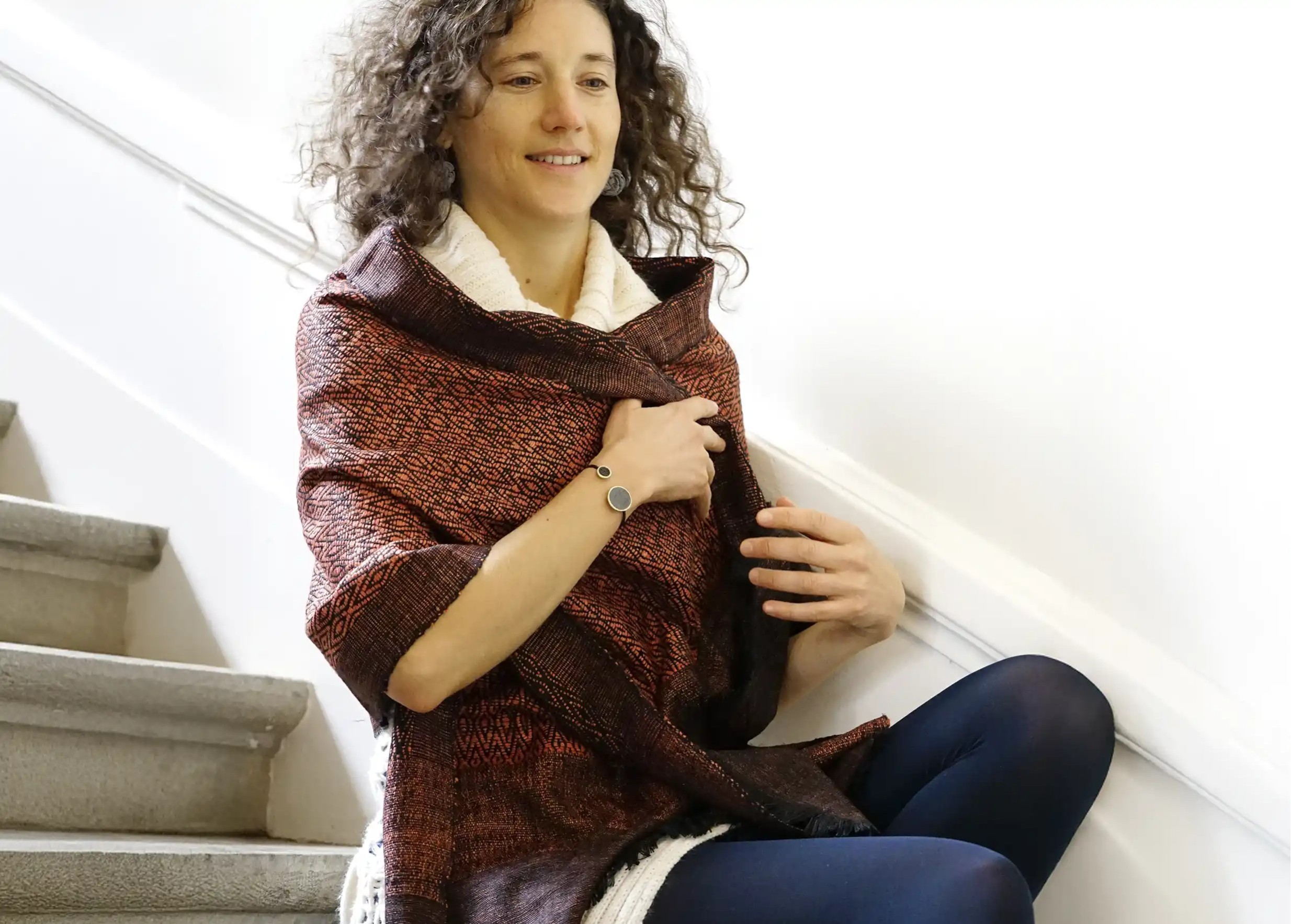 Smiling woman wearing a clay-coloured Eri Eshani wild silk stole with delicate motifs, illuminated by light