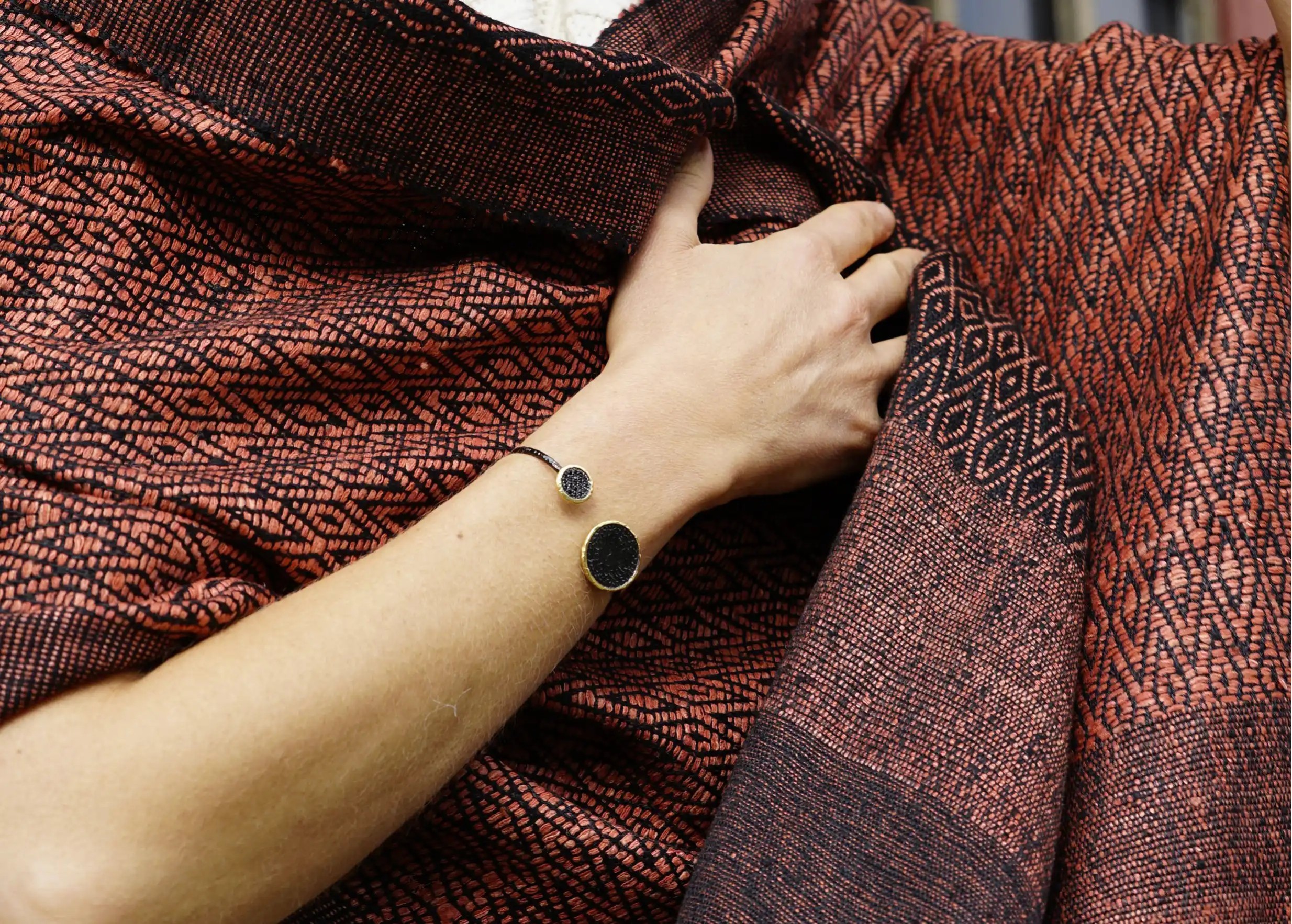 Close-up of a clay-coloured wild silk stole, hand adorned with a Nuit des Temps gold bracelet