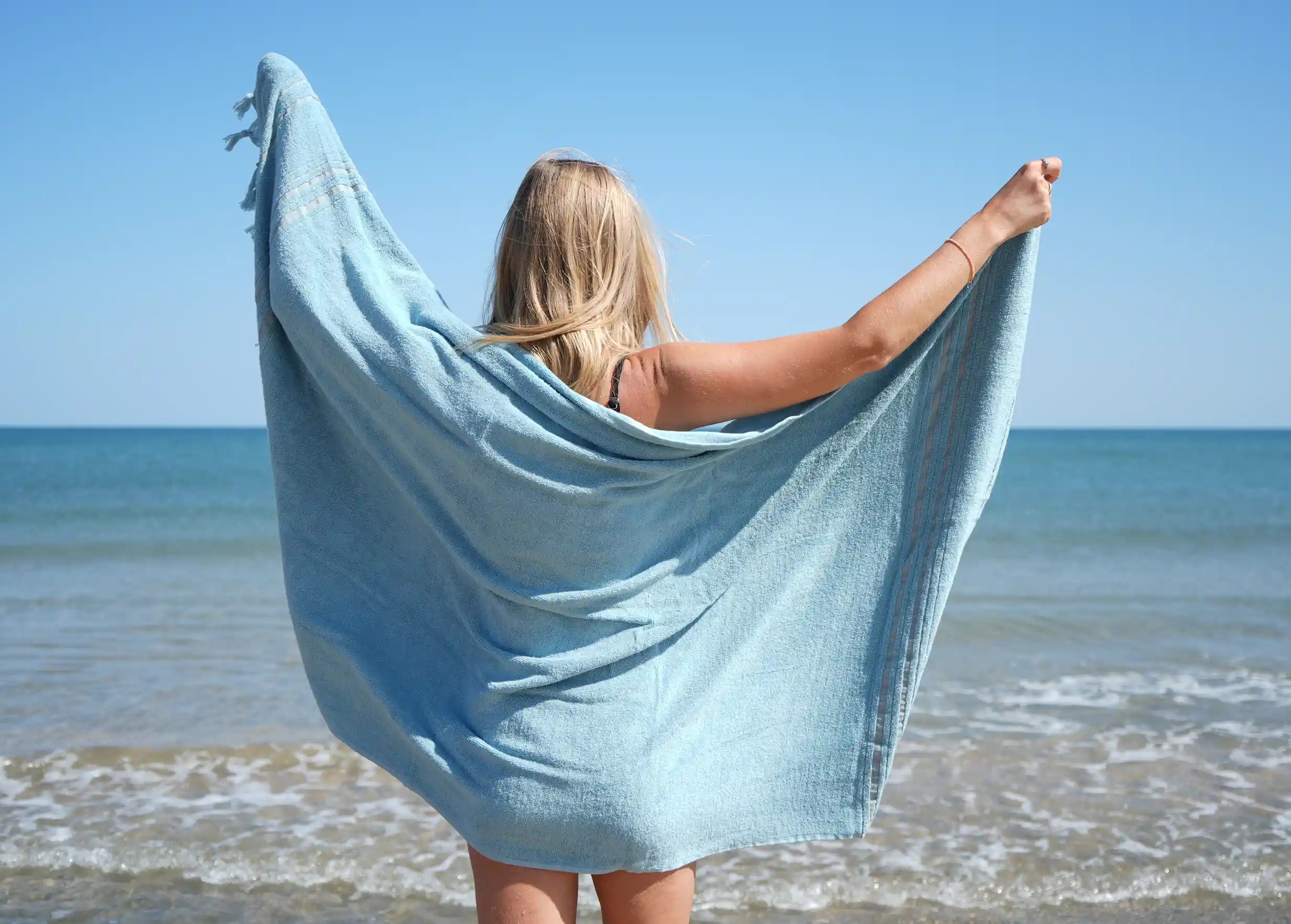 Femme de dos portant une fouta coloris Aigue Marine en coton bio de la marque Karawan