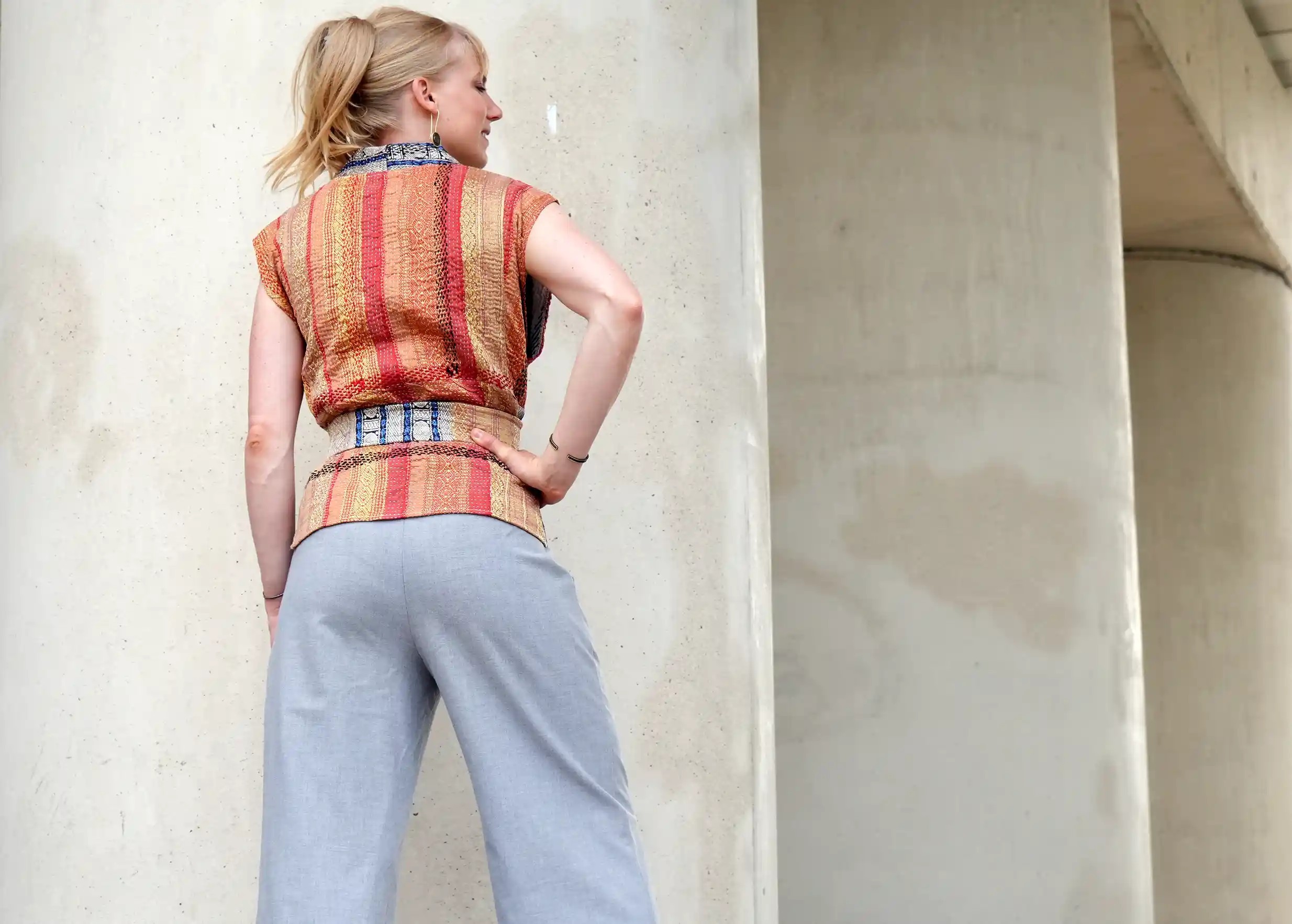 Femme de dos portant un gilet en soie et coton kanta, la main sur sa hanche, regardant sur sa droite