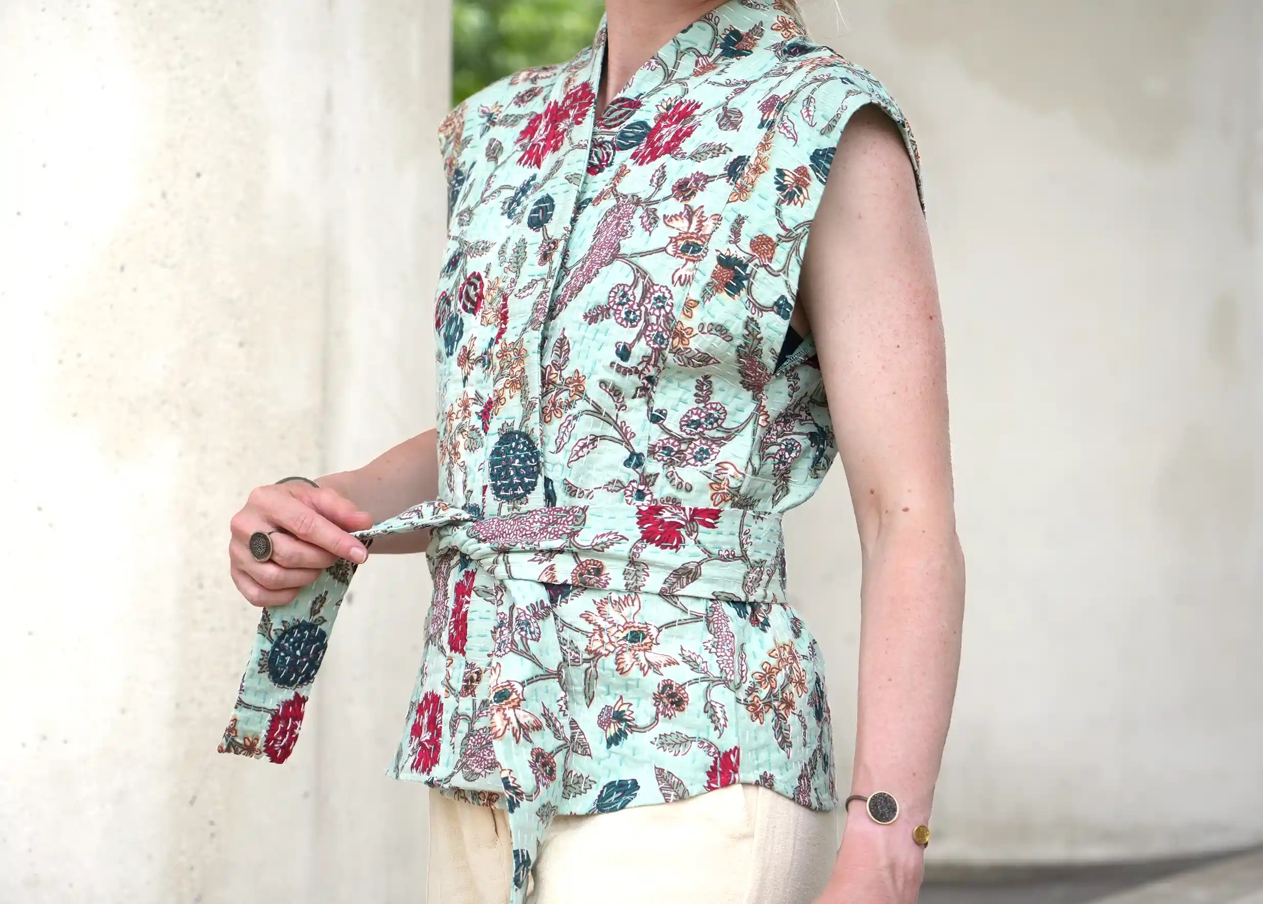 Woman holding the belt of a sleeveless kimono waistcoat, unisex, in quilted cotton, with her fingertips.