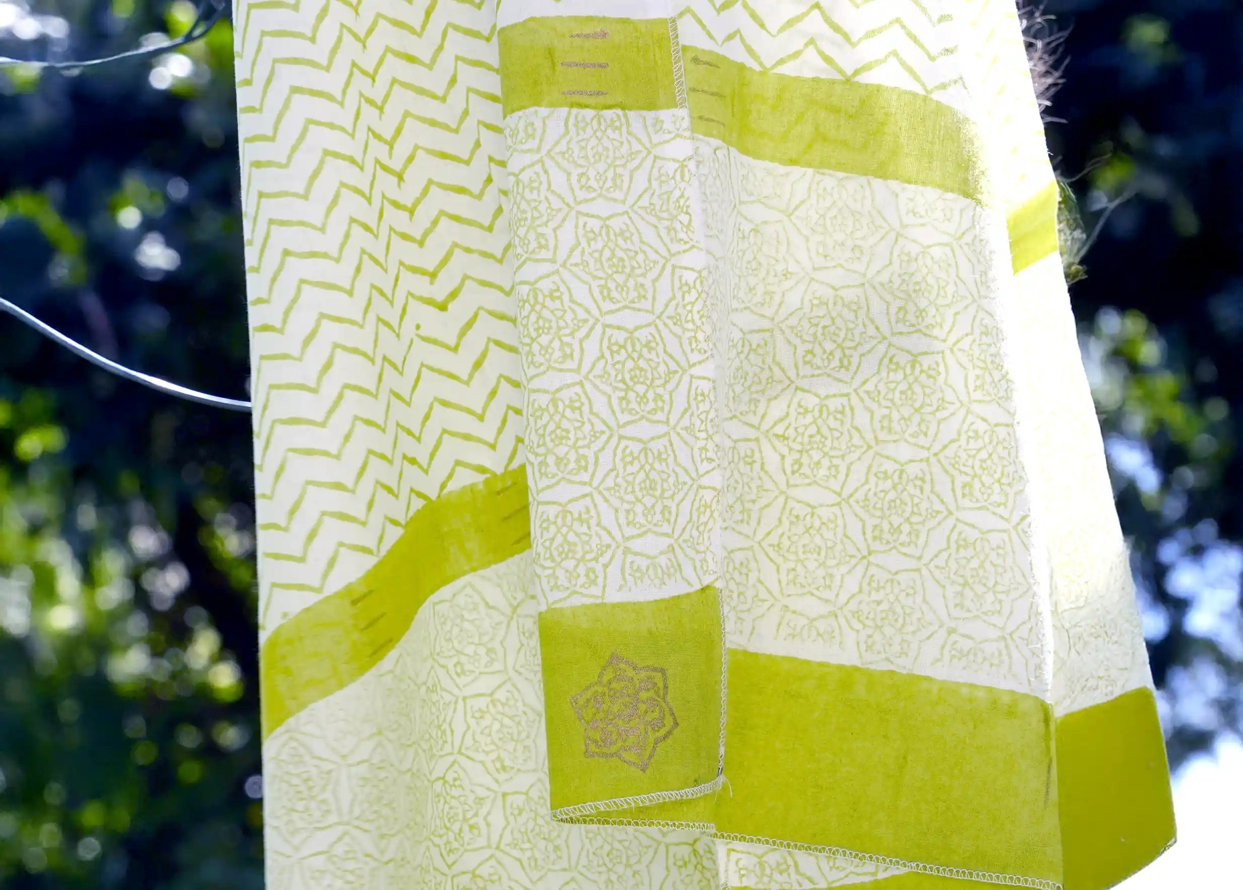 Zigblock cotton sarong with blockprint, bamboo green, floating in the wind, leaves nearby