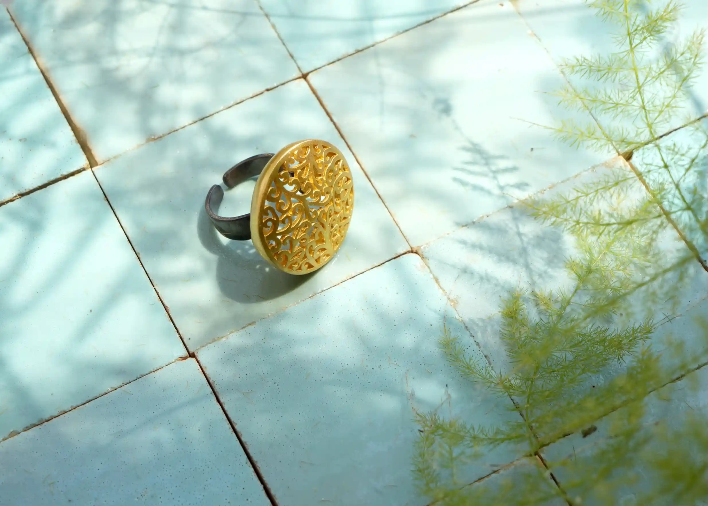 Bague en laiton de la collection Jardin secret posée à plat sur une surface éclairée par la lumière