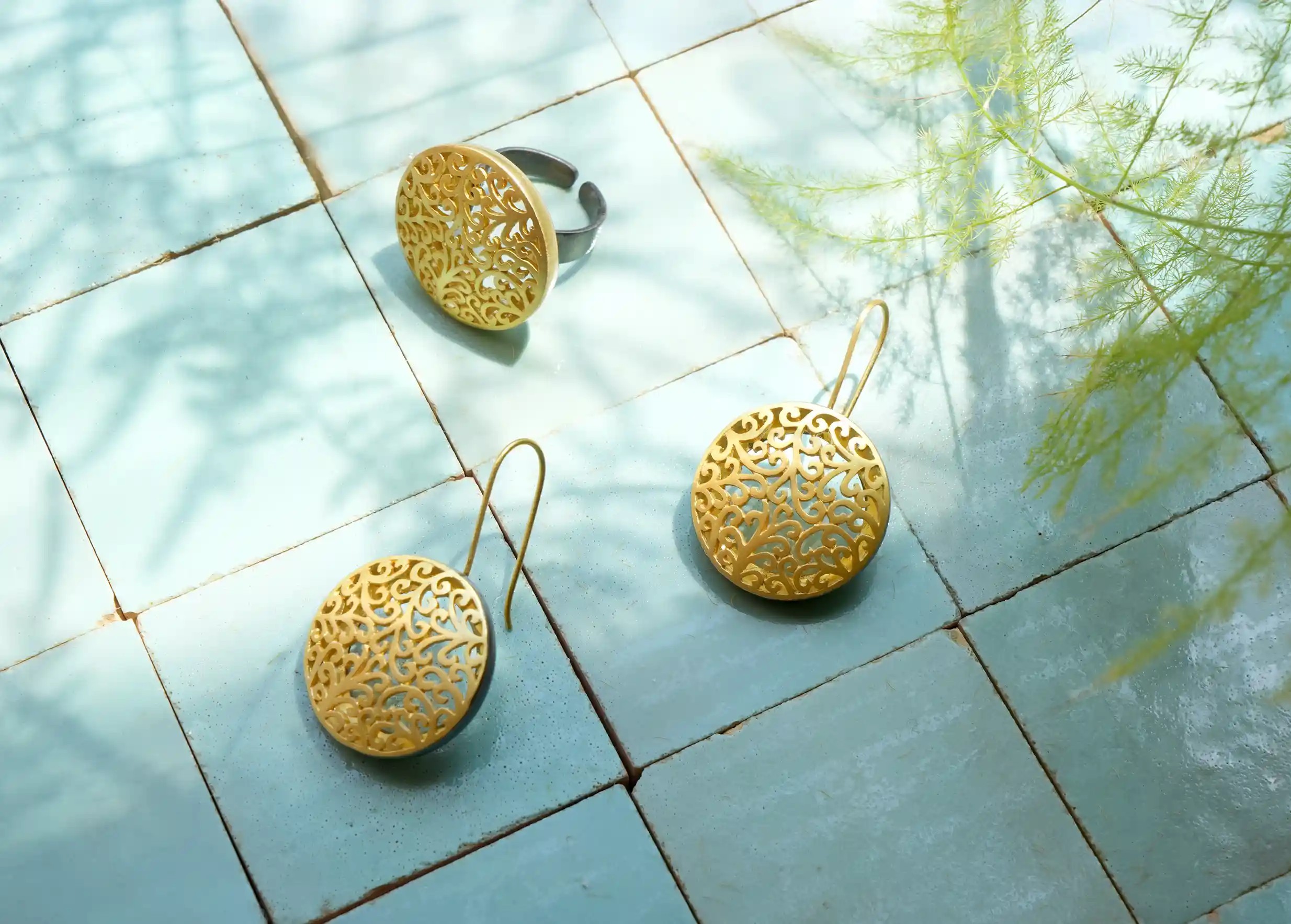 Bague de la collection Jardin Secret en laiton au design ajouré, projetant des ombres sur des carreaux turquoise