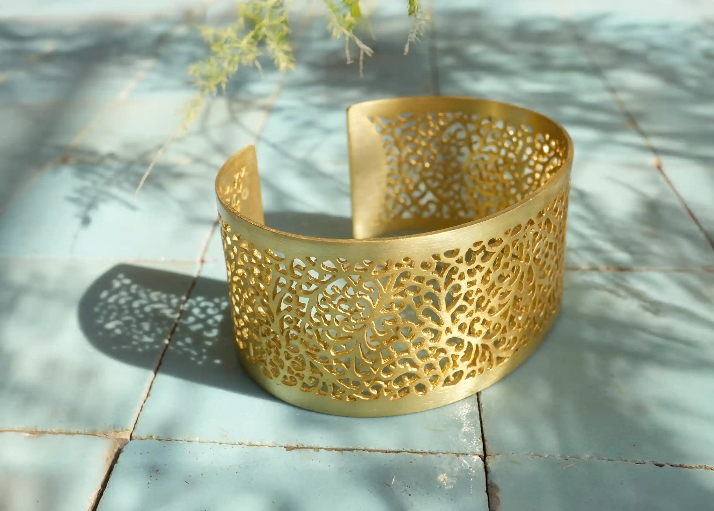 Karawan gilded-plated brass cuff from the Secret Garden collection placed on a tiled surface