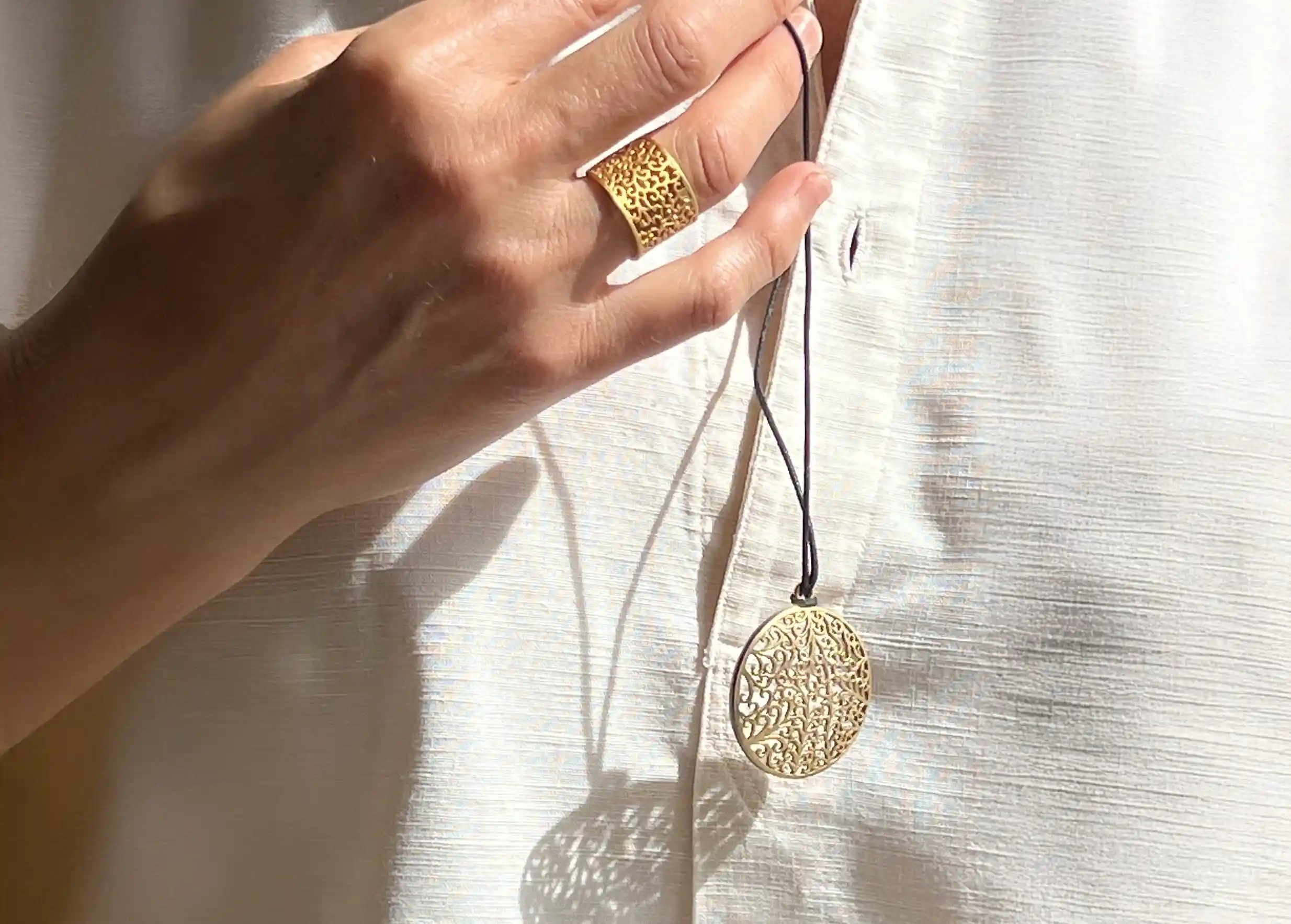 Pendentif en laiton couleur or de la gamme Jardin secret, porté autour du cou et assorti à une bague