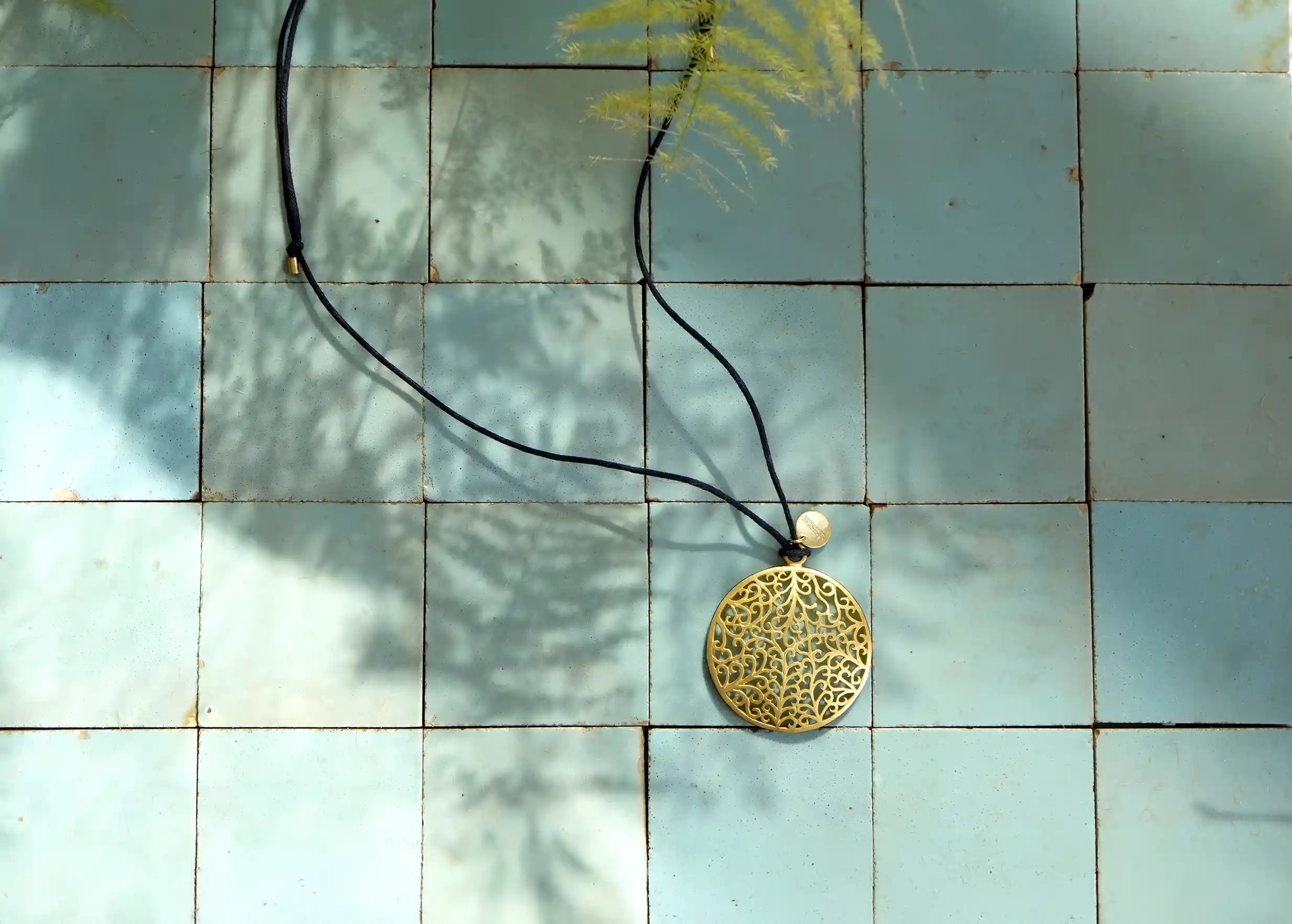 Pendentif en laiton de la gamme Jardin secret, vus en hauteur sur une surface à carreaux