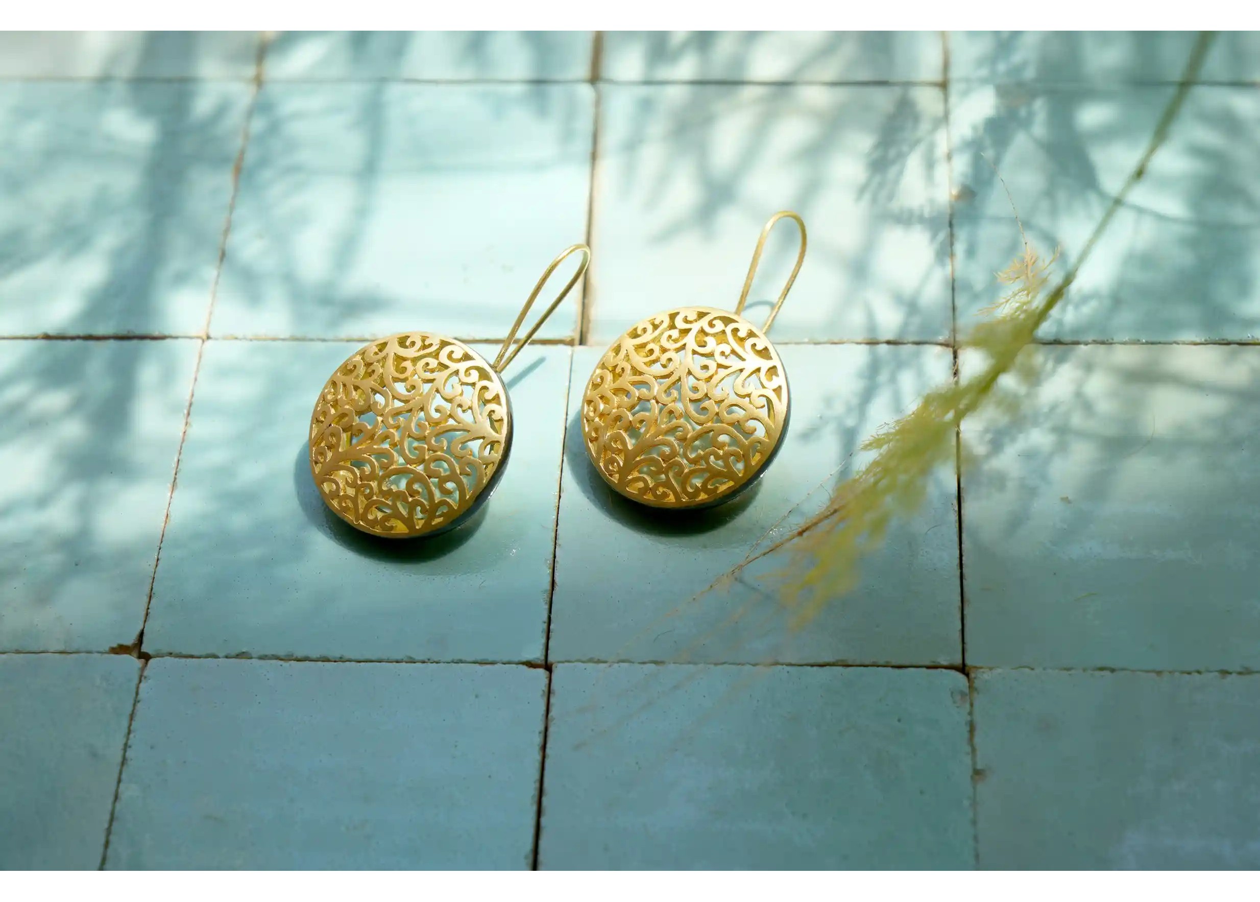 Boucles d'oreilles en laiton de la gamme Jardin secret, avec effet doré, posées sur des carreaux bleus