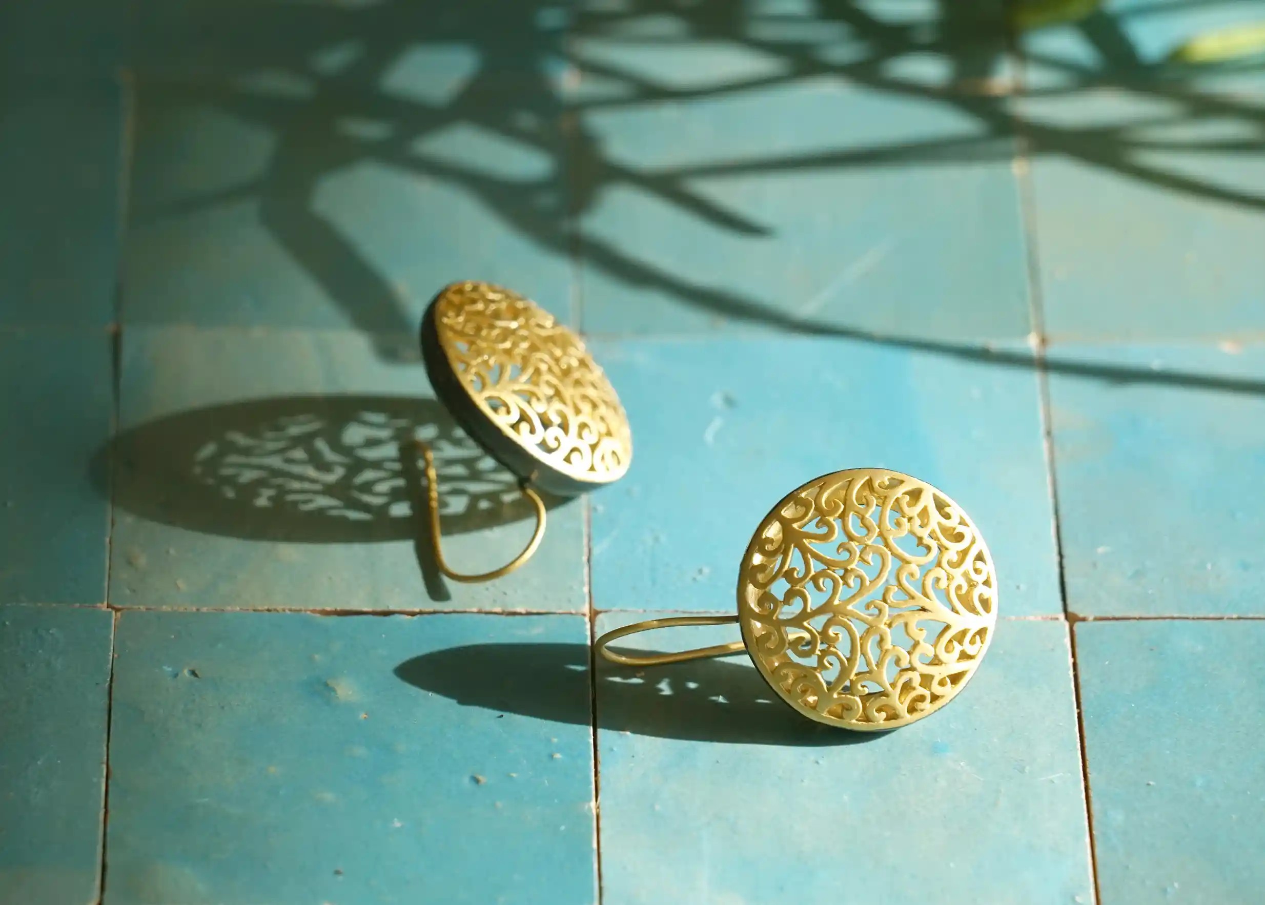 Boucles d'oreilles en laiton doré de la gamme Jardin secret par Karawan, posées sur des carreaux bleus