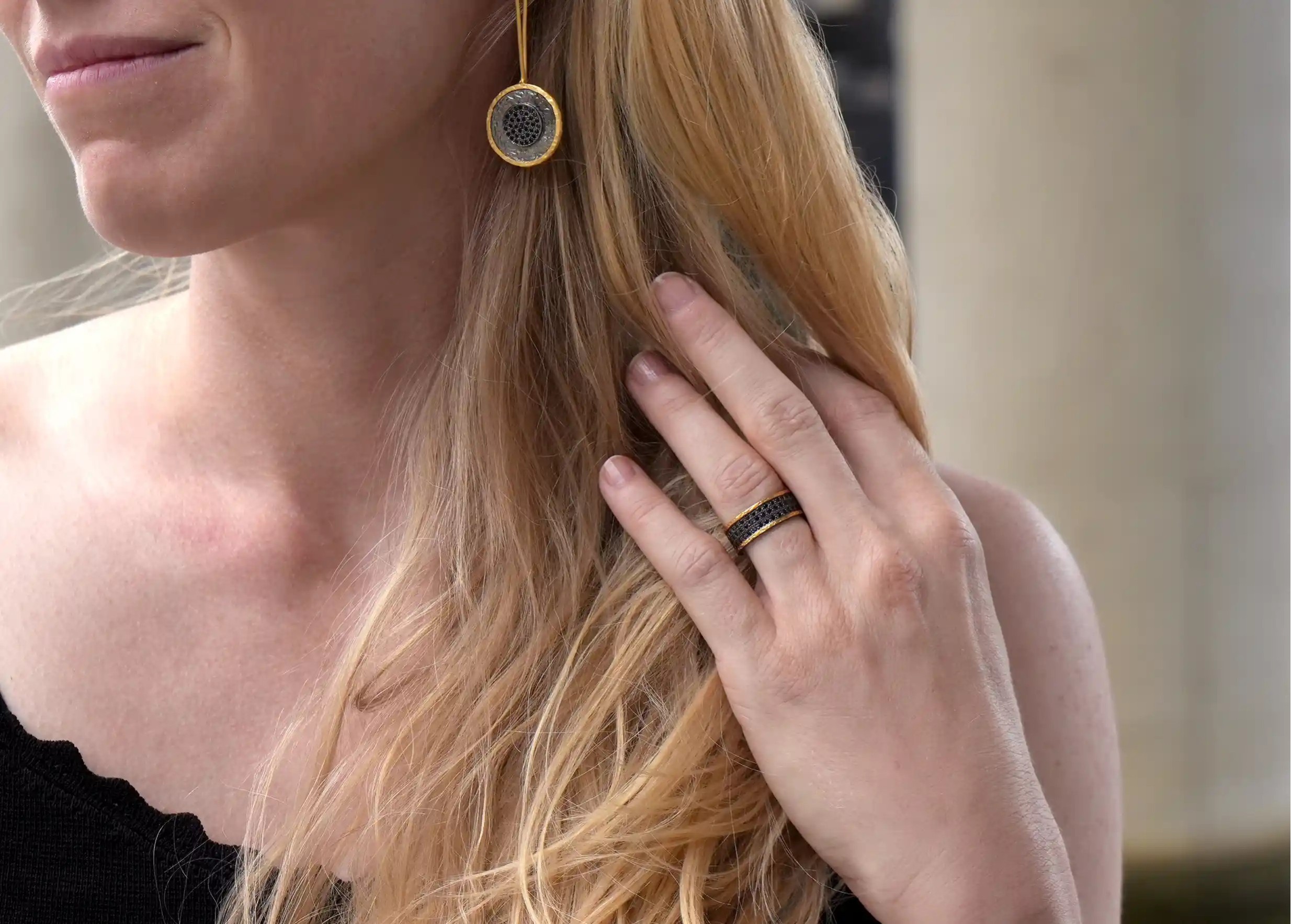 Woman wearing an adjustable ring and brass and zirconium earrings, Dawn of Time collection