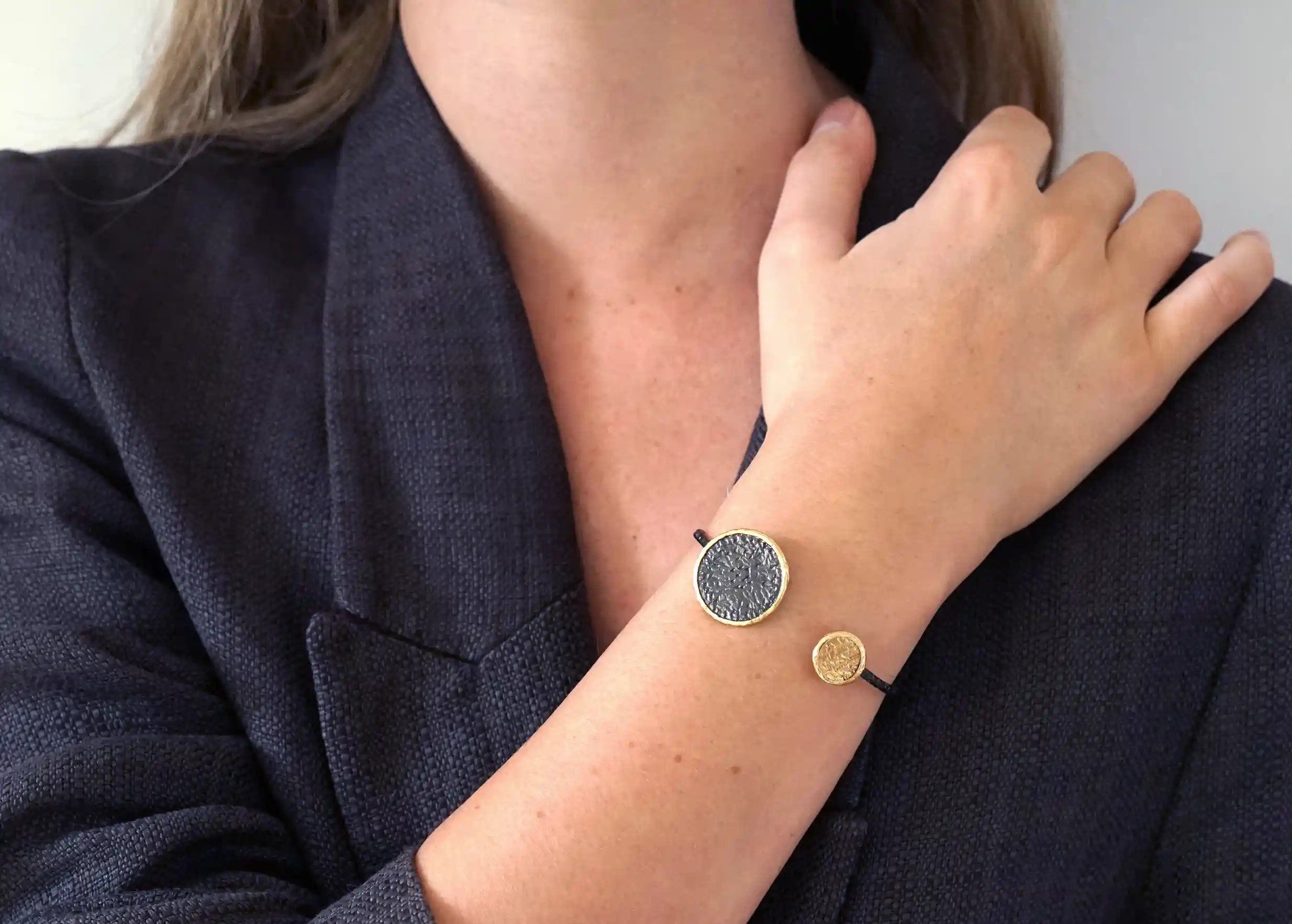 Bangle bracelet from the Dawn of Time collection in brass and zirconium, handcrafted, worn around the wrist indoors.