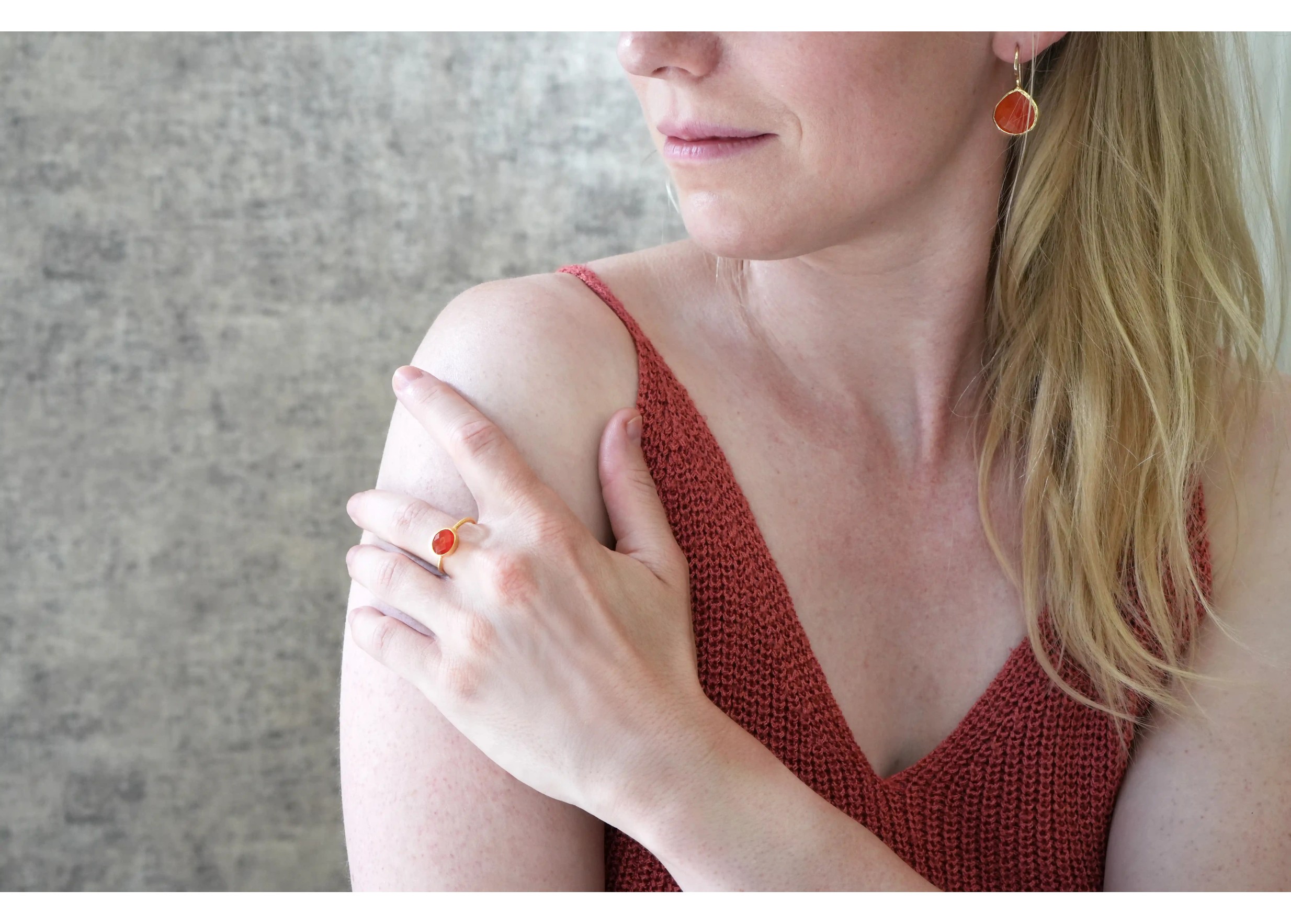 Woman wearing earrings and a gold-plated ring with a drop and carnelian stone from the Karawan Authentic brand.
