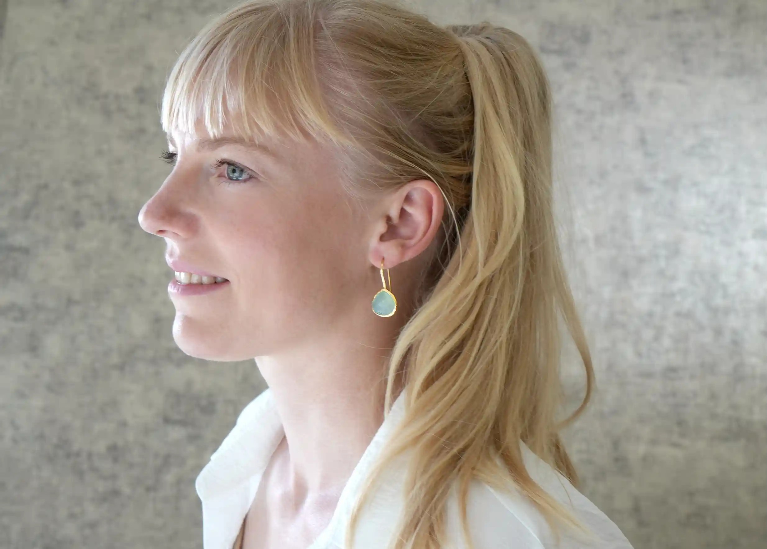 Femme de profil portant les boucles d’oreilles « Drop » or & pierre calcédoine, collection Yamuna