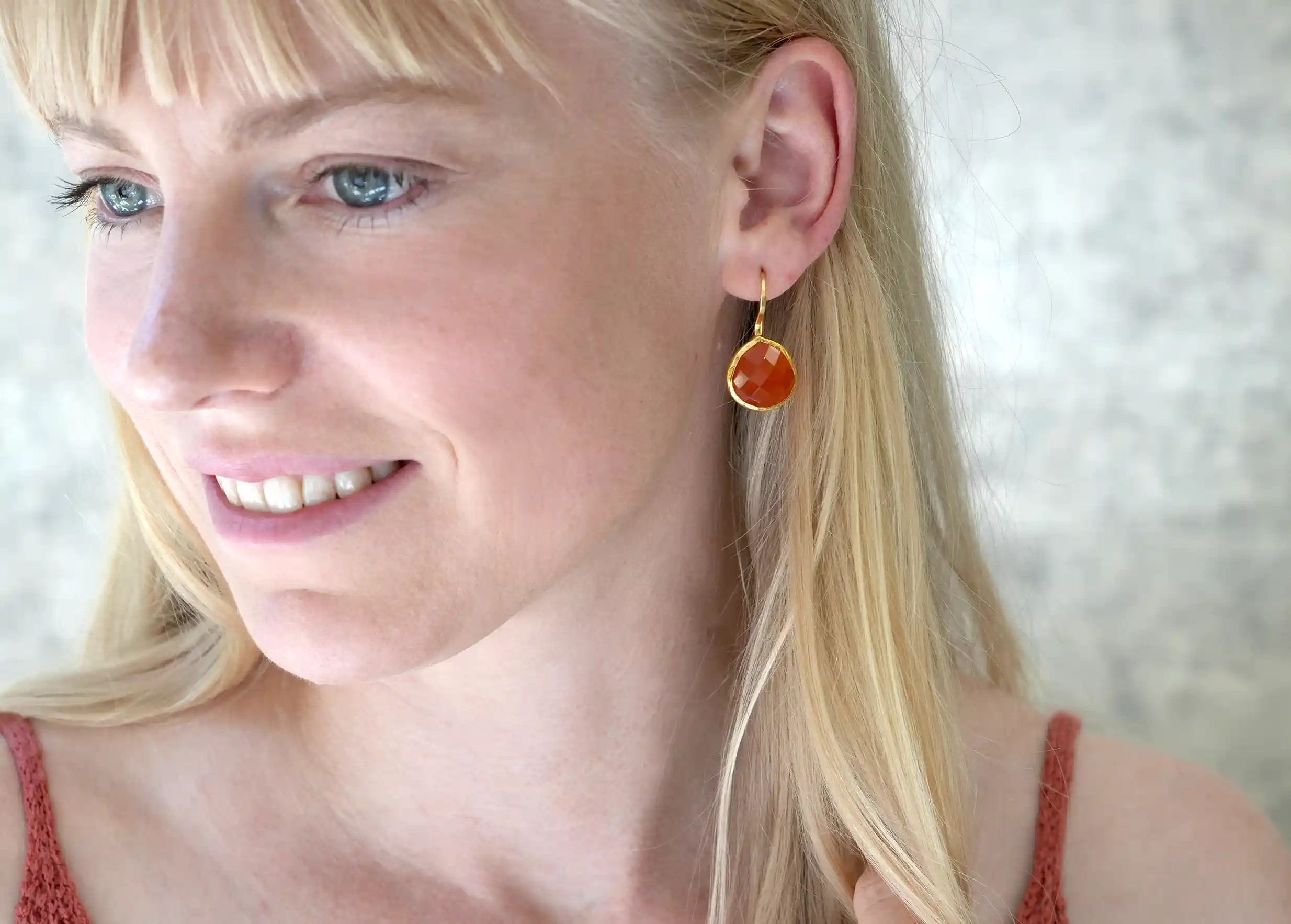 Smiling woman wearing gold and carnelian drop earrings, Yamuna collection
