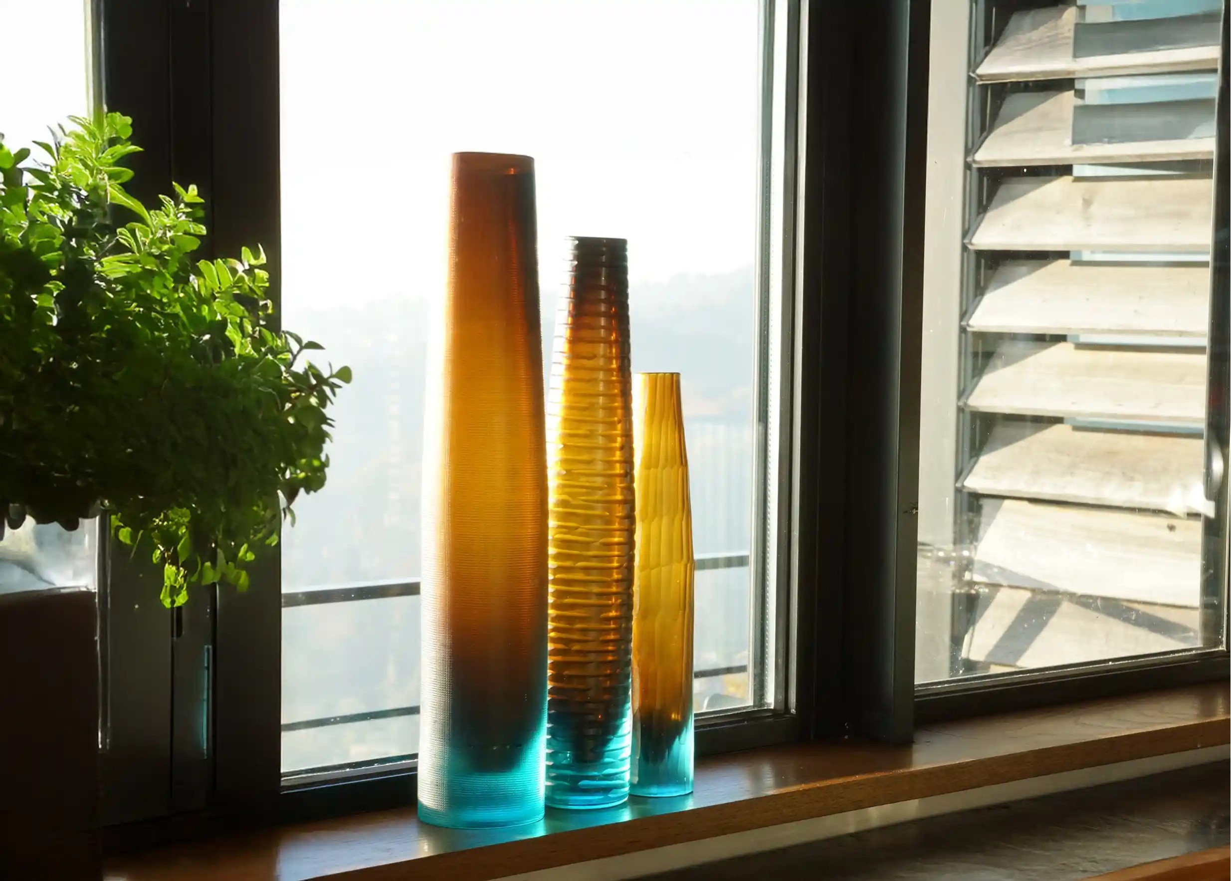 Ensemble de vase bicolore turquoise et ambre en verre recyclé près d'une fenêtre, soufflé à la bouche, collection Flower