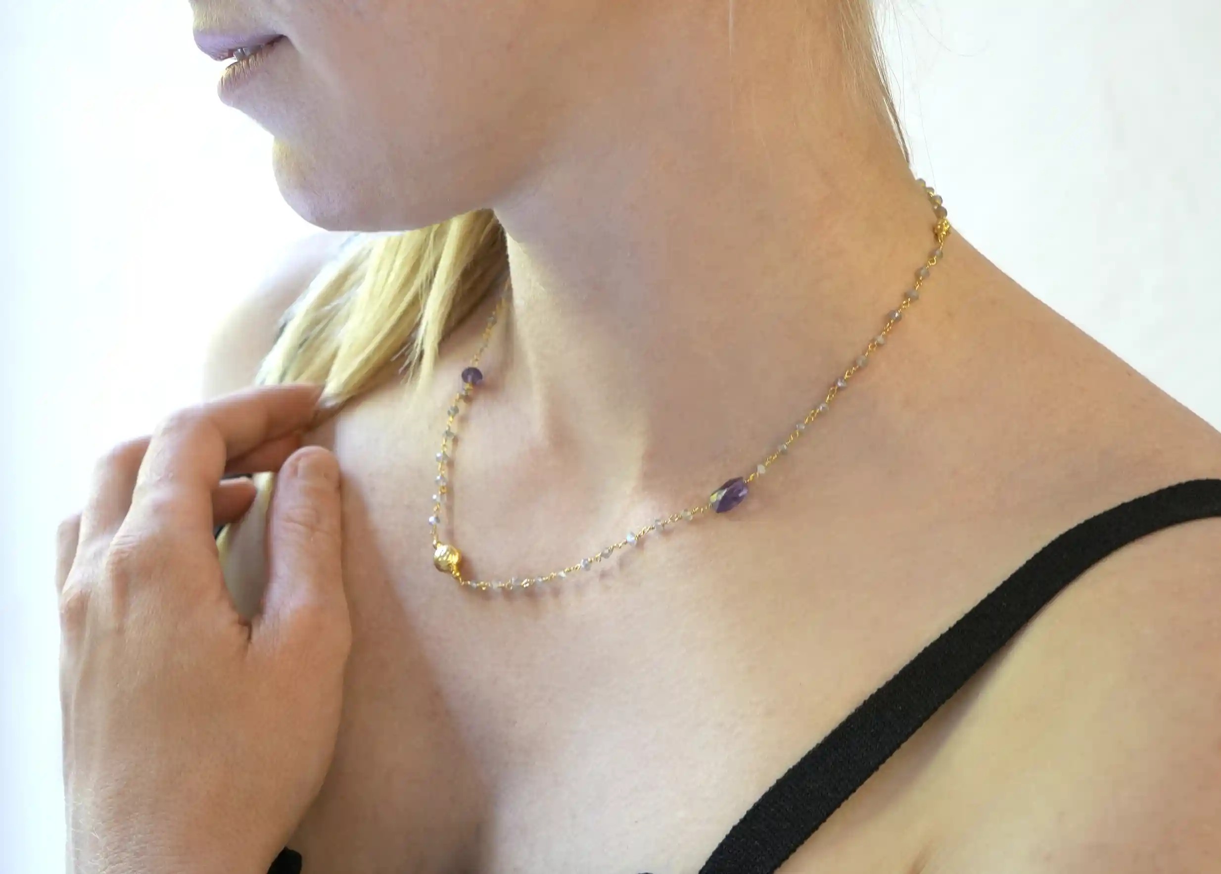 ‘Ani’ necklace in gold with amethyst and labradorite stones, worn by a woman indoors