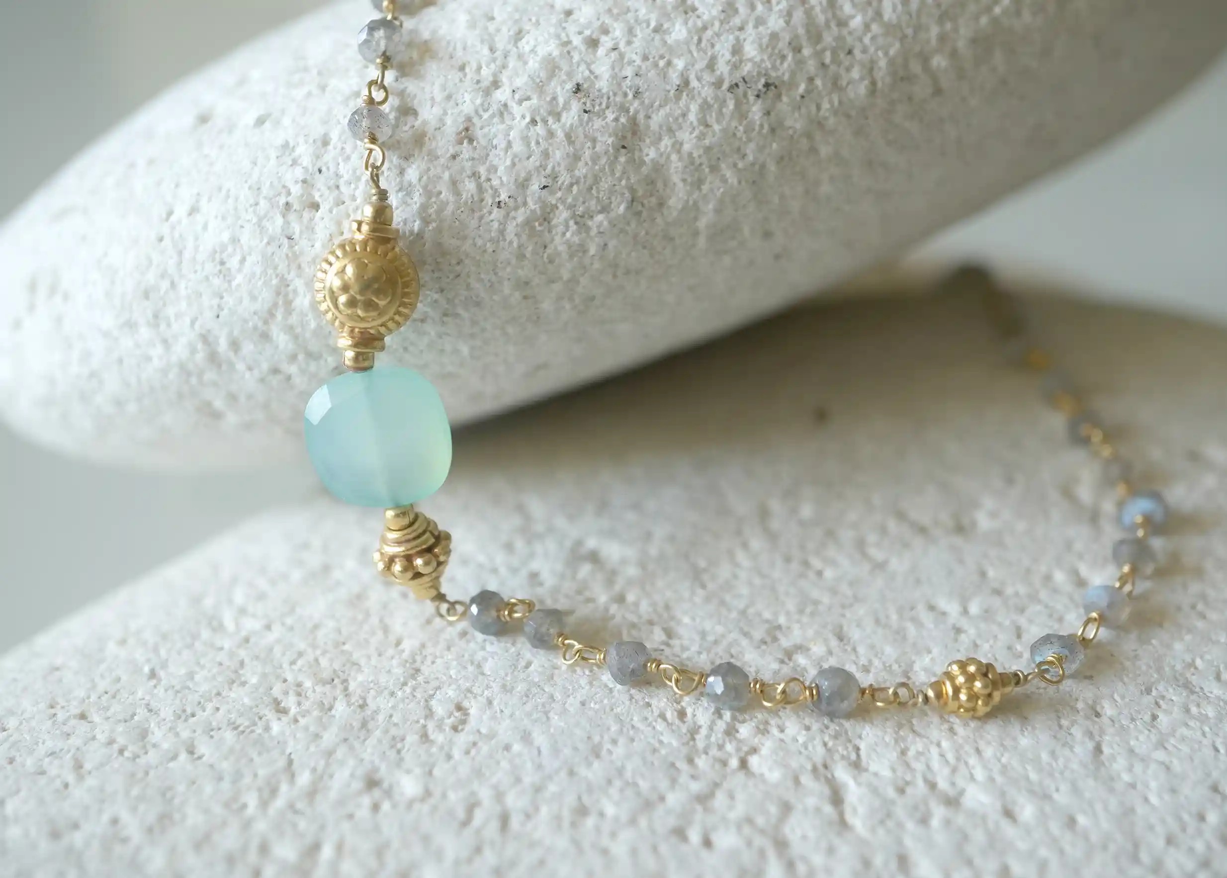 Focus on the details of the ‘Ani’ gold-plated necklace with aqua chalcy and labradorite stones, from the Yamuna collection.
