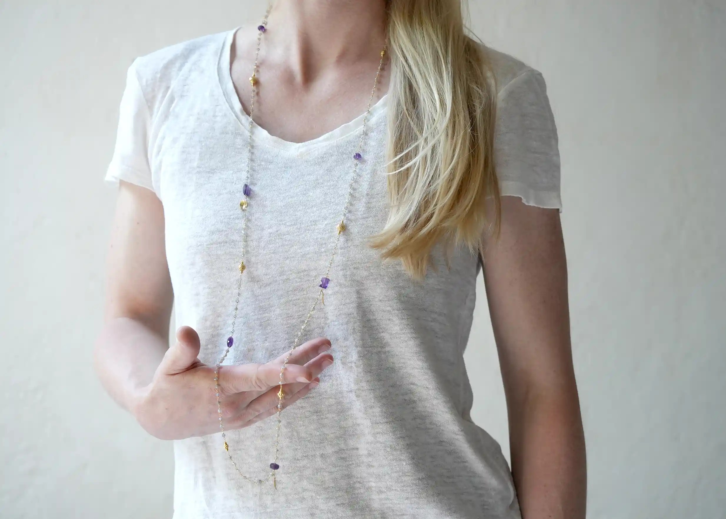 Woman wearing an ‘Ani’ necklace in gold with amethyst and labradorite stones, from the Yamuna collection.