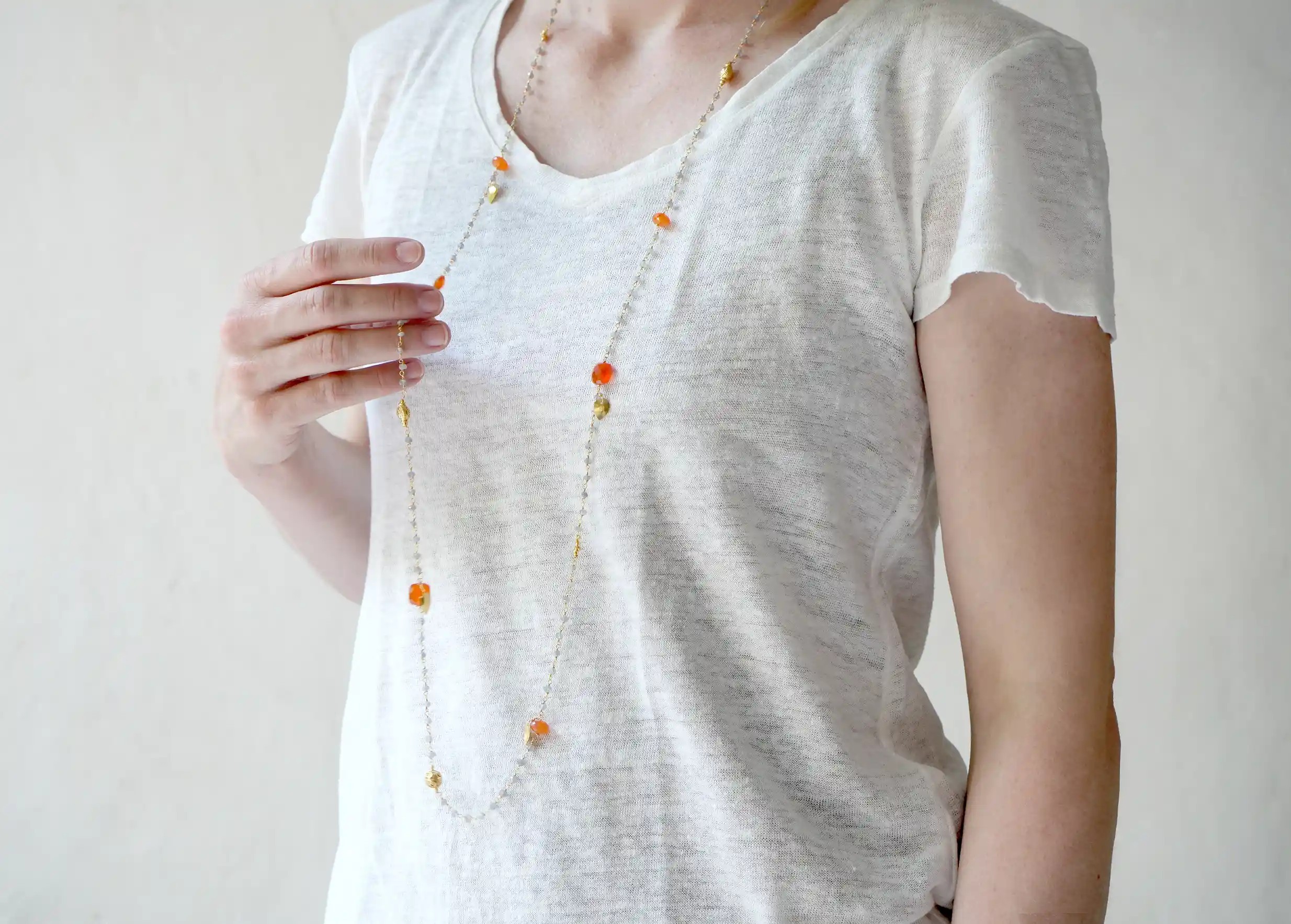 Sautoir « Ani » Or & pierres de cornaline et labradorite, enroullé autour des doigts d'une femme