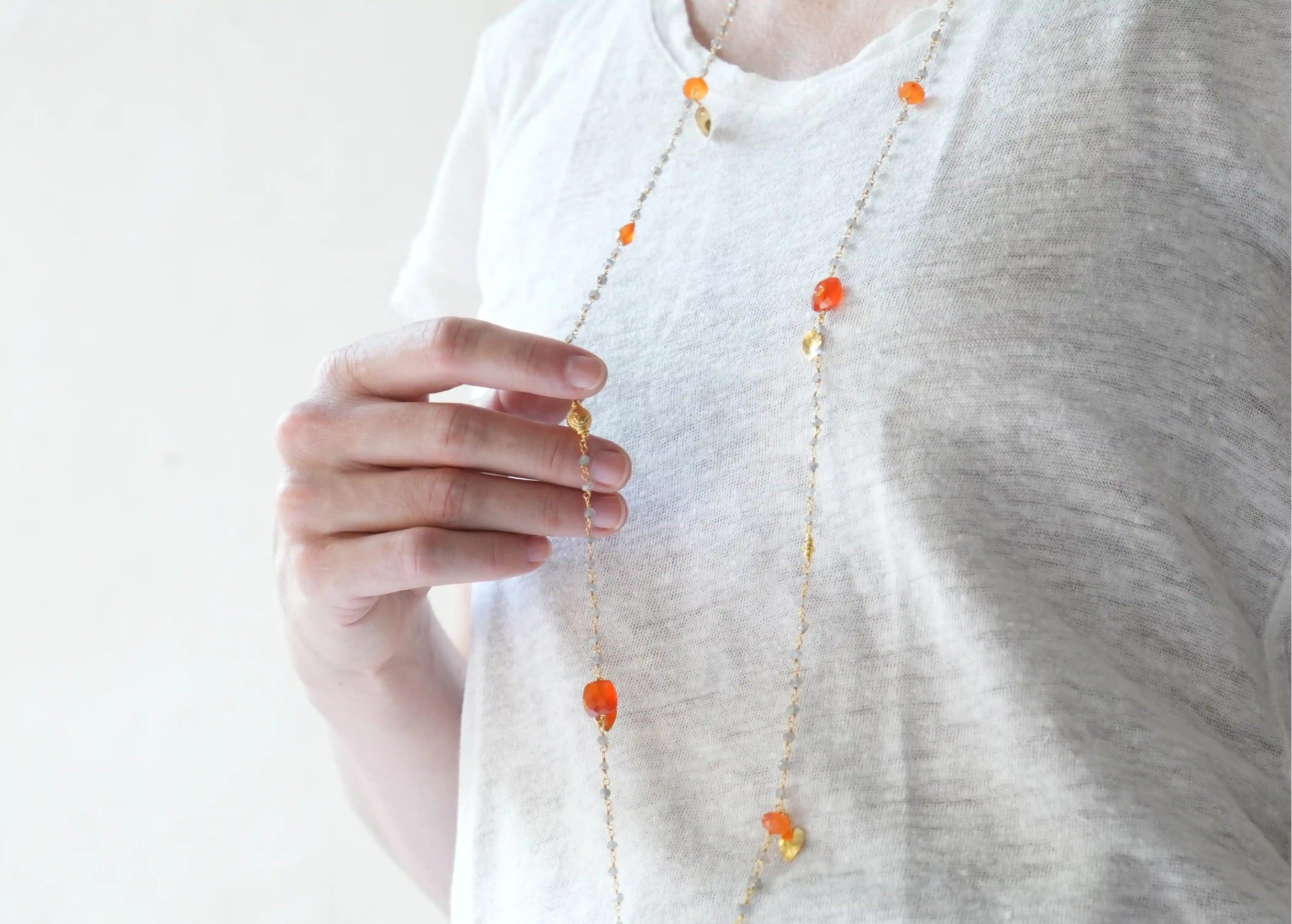 ‘Ani’ gold-plated necklace with carnelian and labradorite stones, worn by a woman indoors