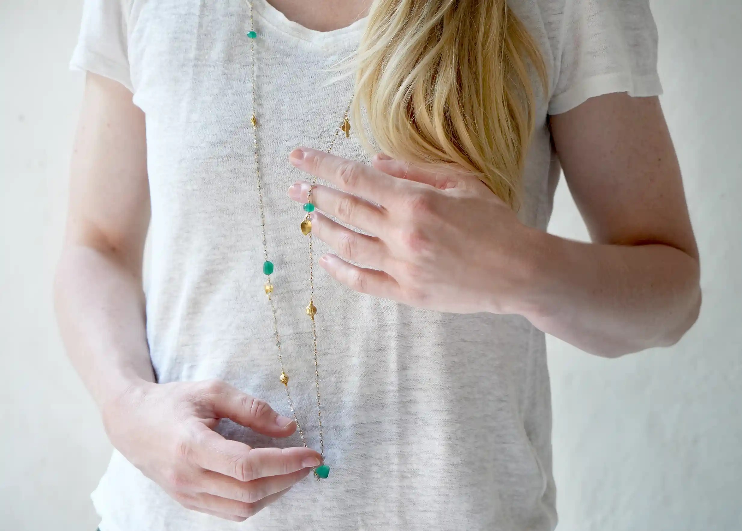 ‘Ani’ gold-plated necklace with green onyx and labradorite stones, wrapped around a woman's fingers