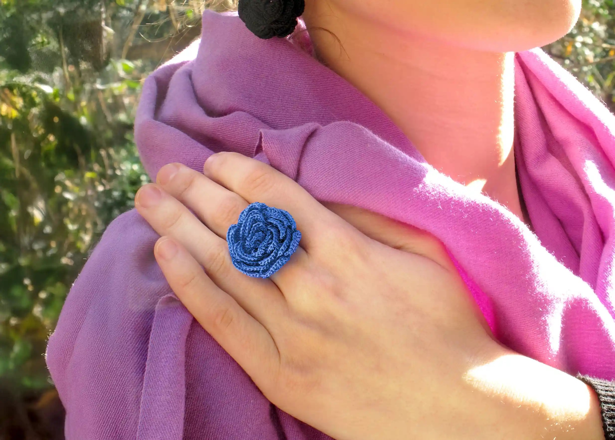 Bague en dentelle bleue par Karawan, portée au doigt par une femme en extérieur