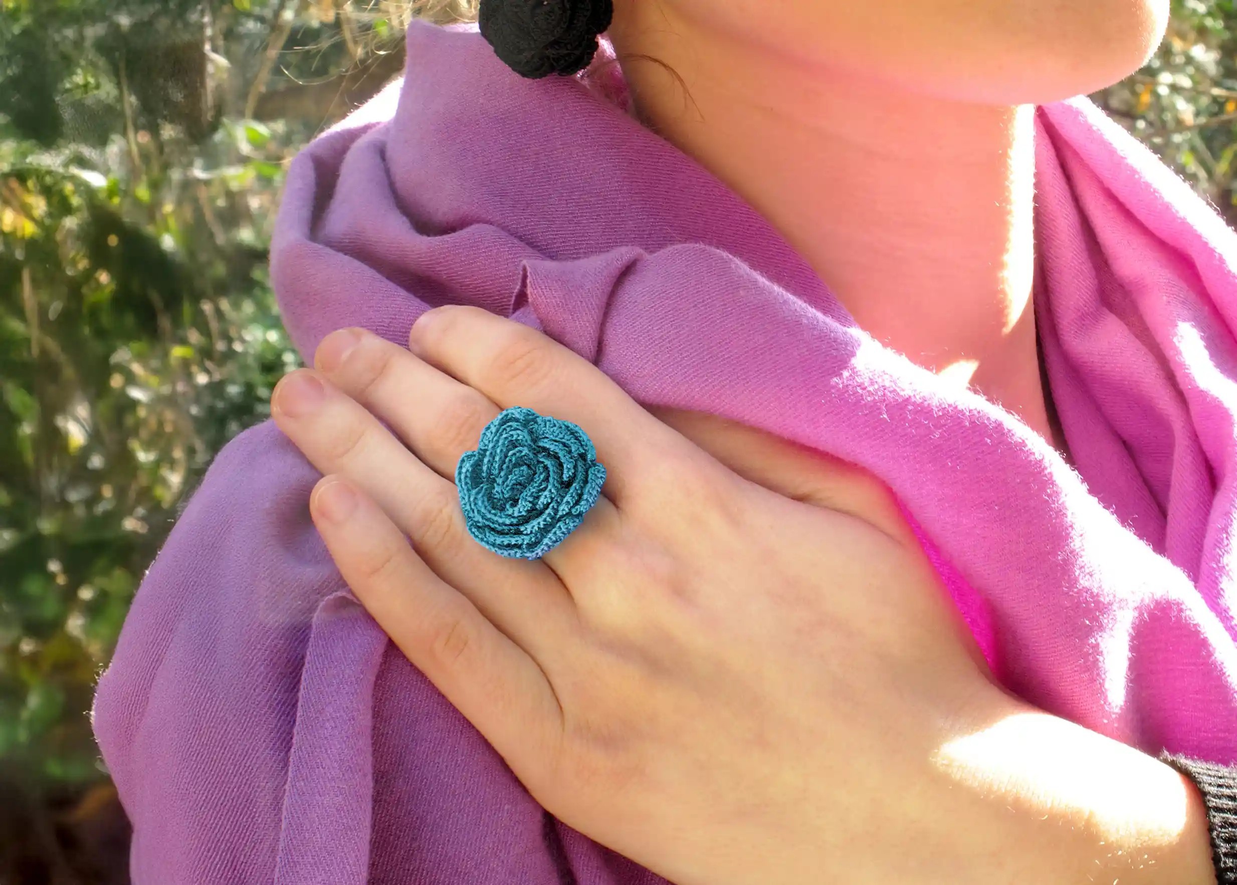 Woman outdoors wearing a Beklis lagoon-coloured lace ring with a twisted floral design