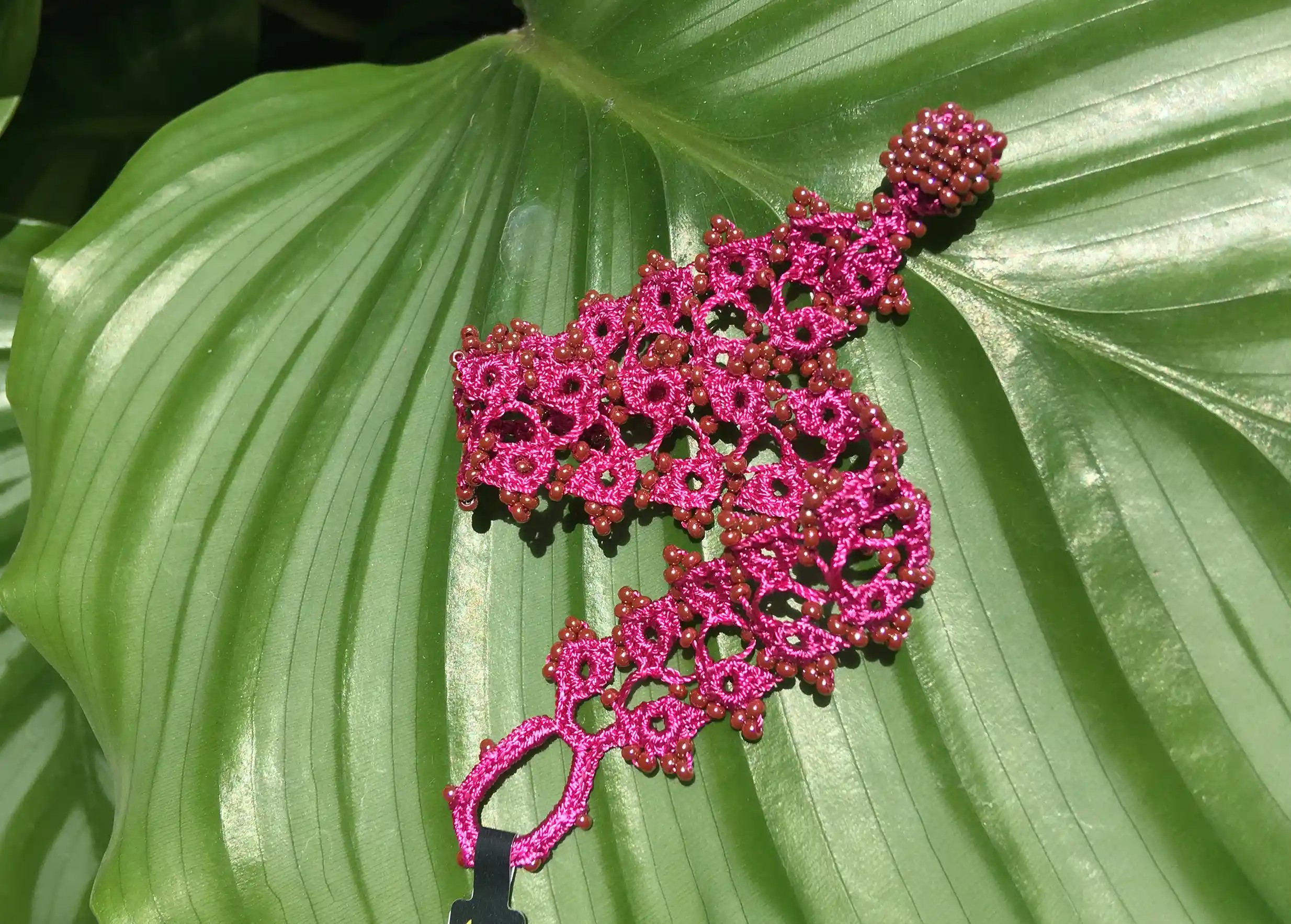 Bracelet en dentelle Husnu Bergamote posé sur une feuille verte, avec des motifs ajourés et des perles
