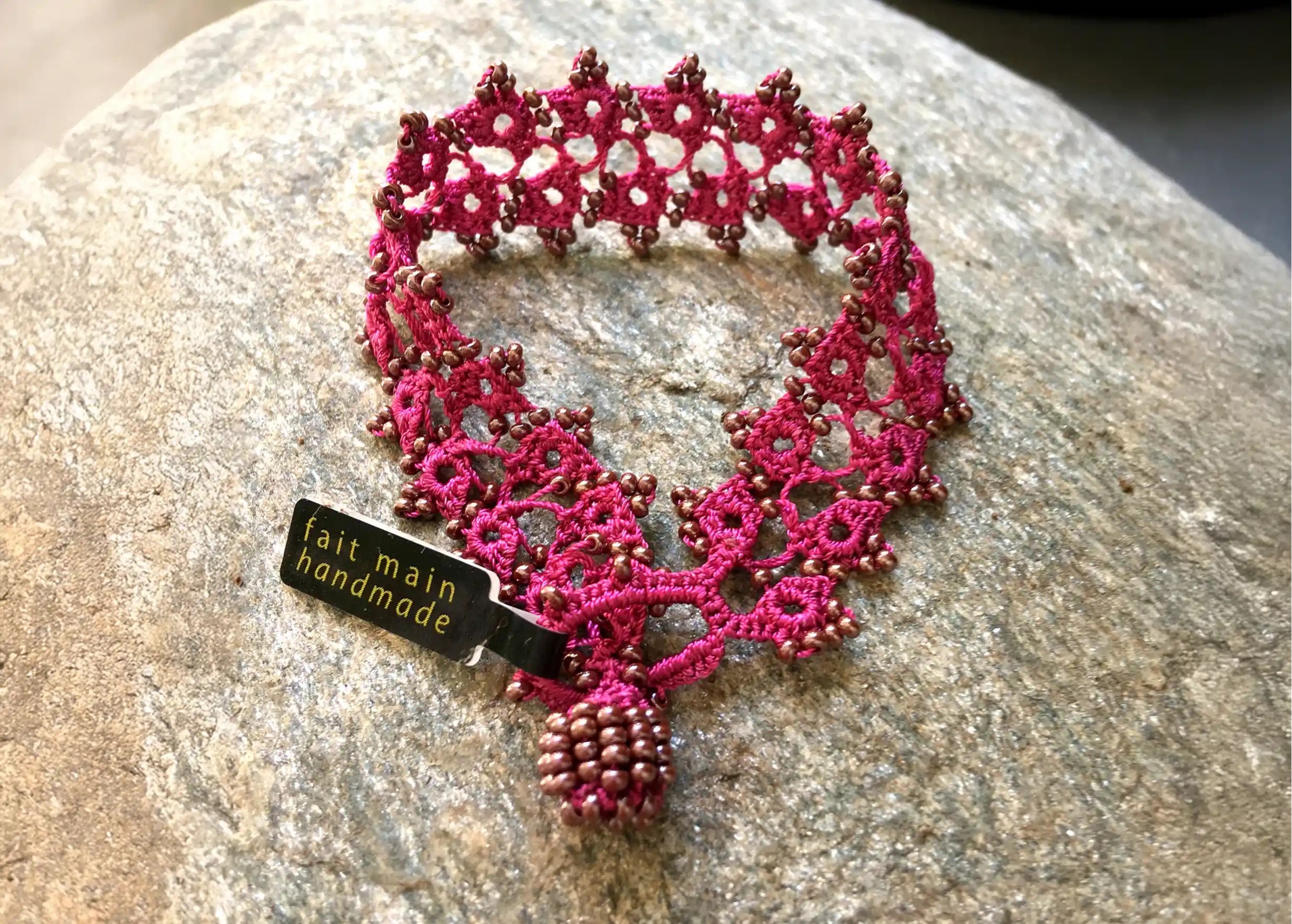 Bracelet en dentelle Husnu rose-violet, sur une surface en pierre avec une étiquette "fait main"