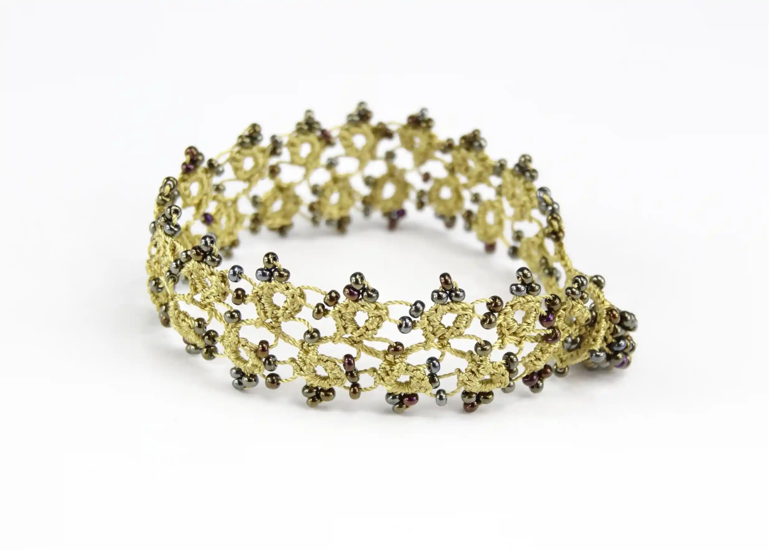 Bracelet en dentelle Husnu couleur vert lichen, avec des perles, posé sur fond blanc