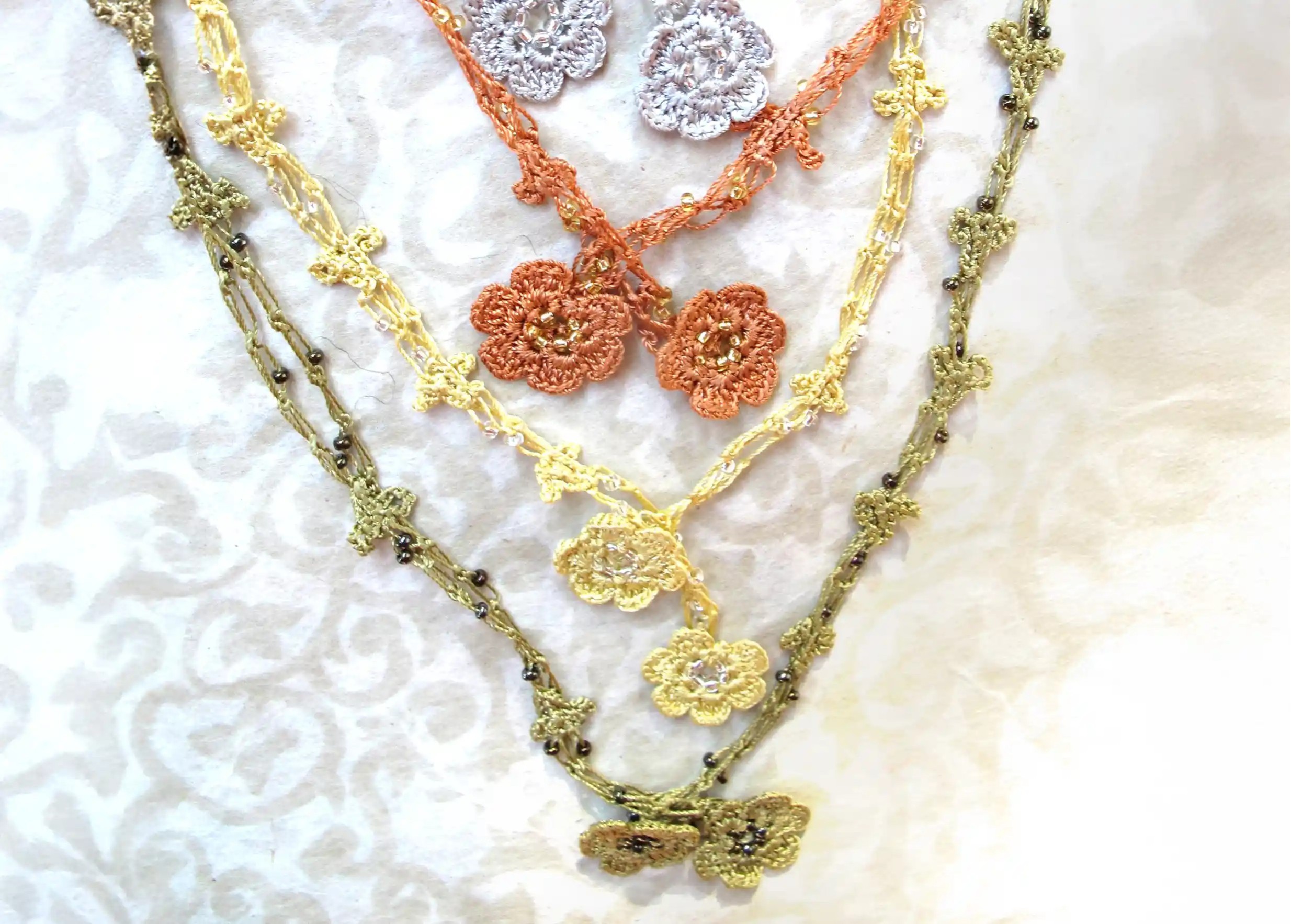 Collection de bracelets-colliers chaînette en dentelle Oya aux motifs floraux, suspendus sur un fond gris