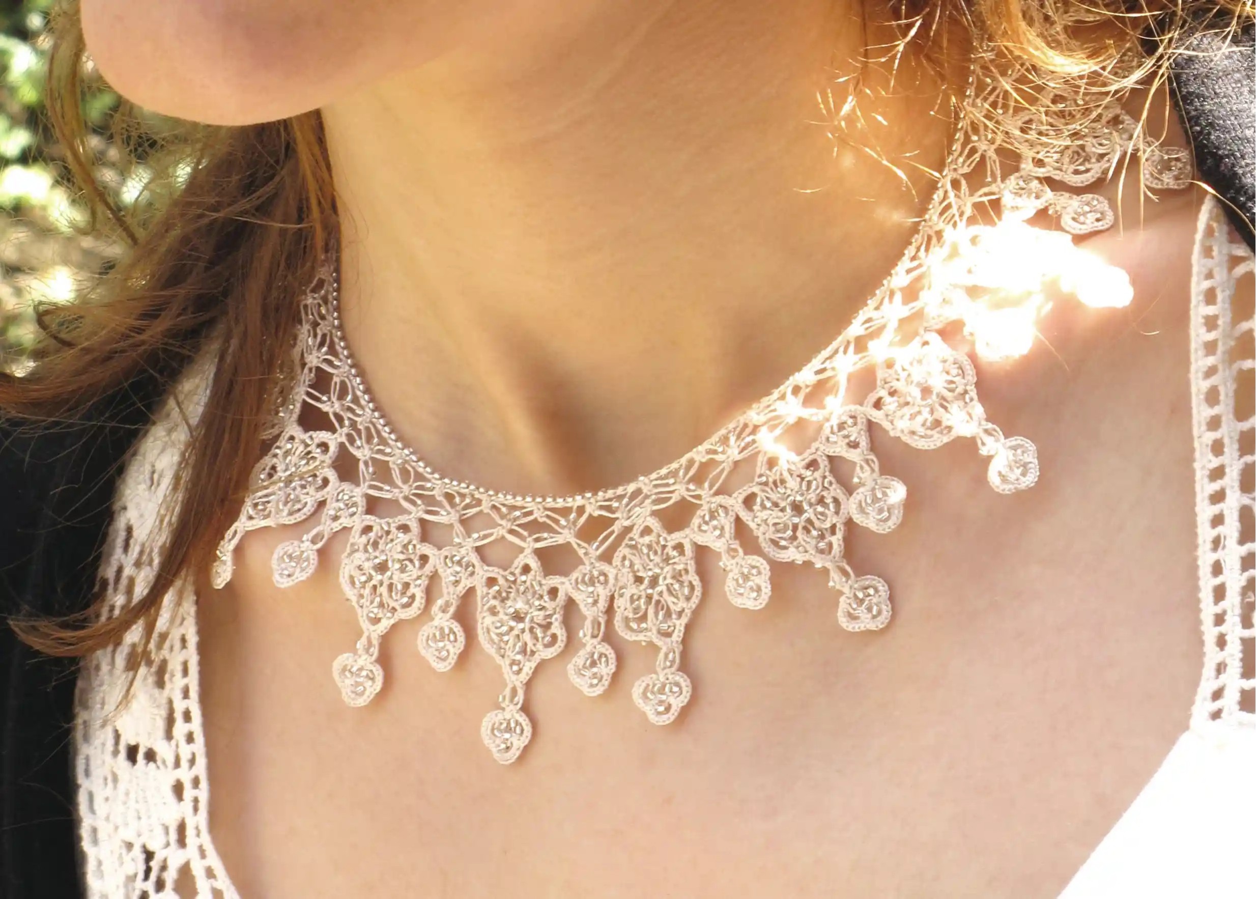 Femme portant un collier Sonya coloris ivoire et une bague en dentelle Oya dans un cadre végétal ensoleillé