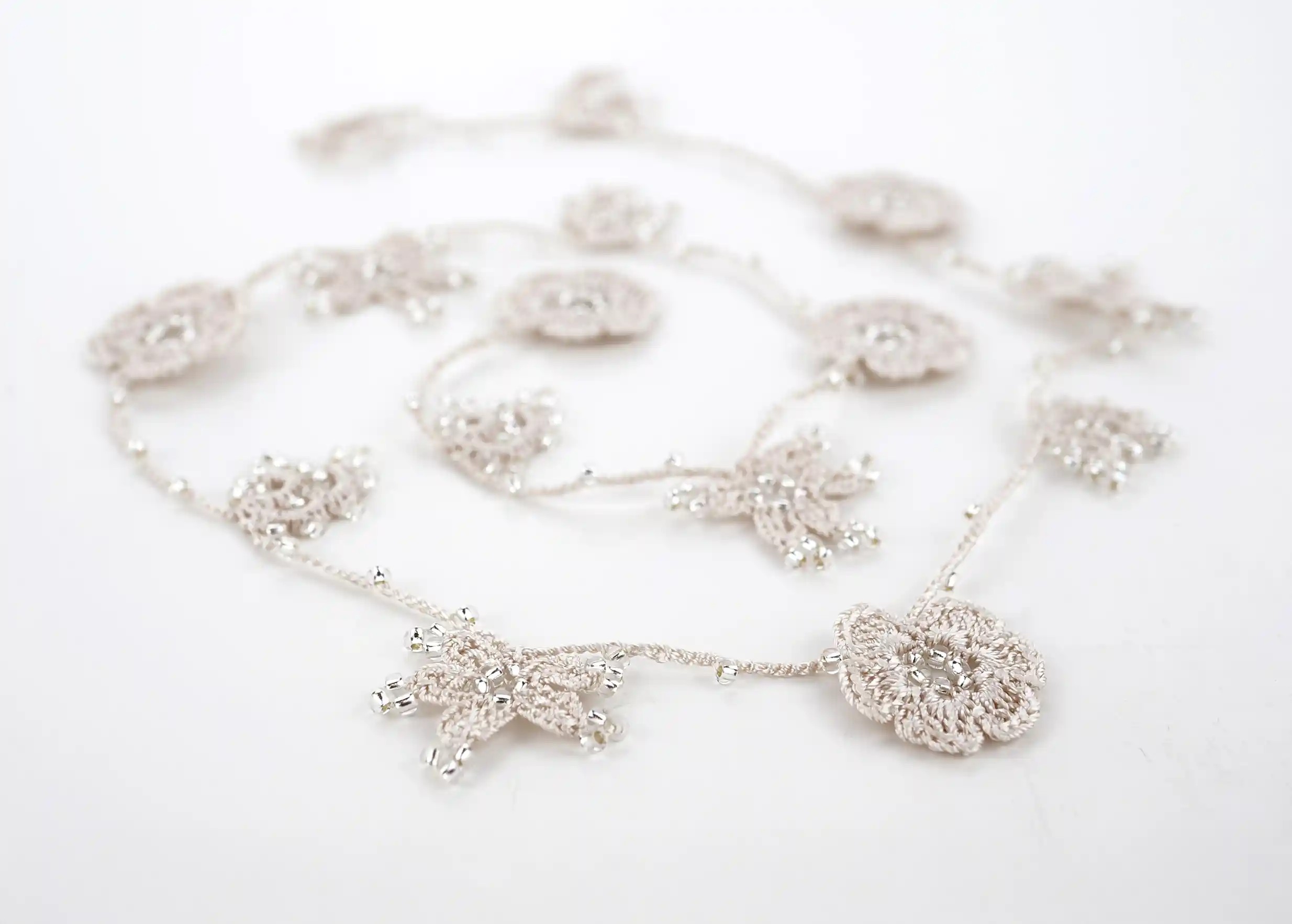 Focus on the design of an ivory-coloured lace necklace, with decorative threads and motifs adorned with pearls.