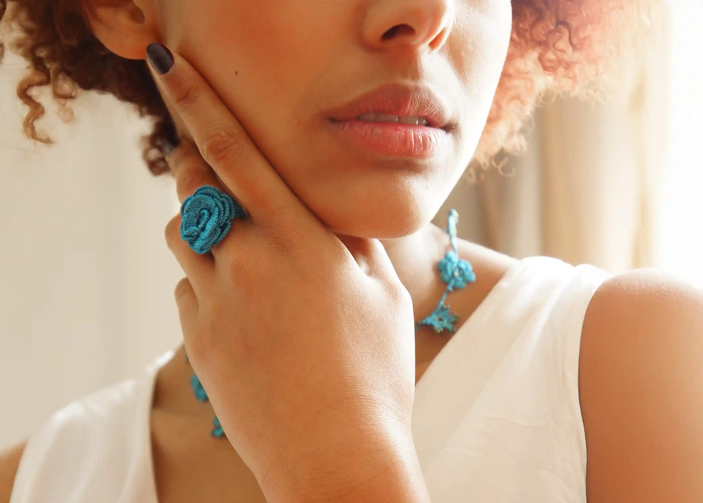 Woman wearing a Beklis lagoon-coloured lace ring with a twisted floral design