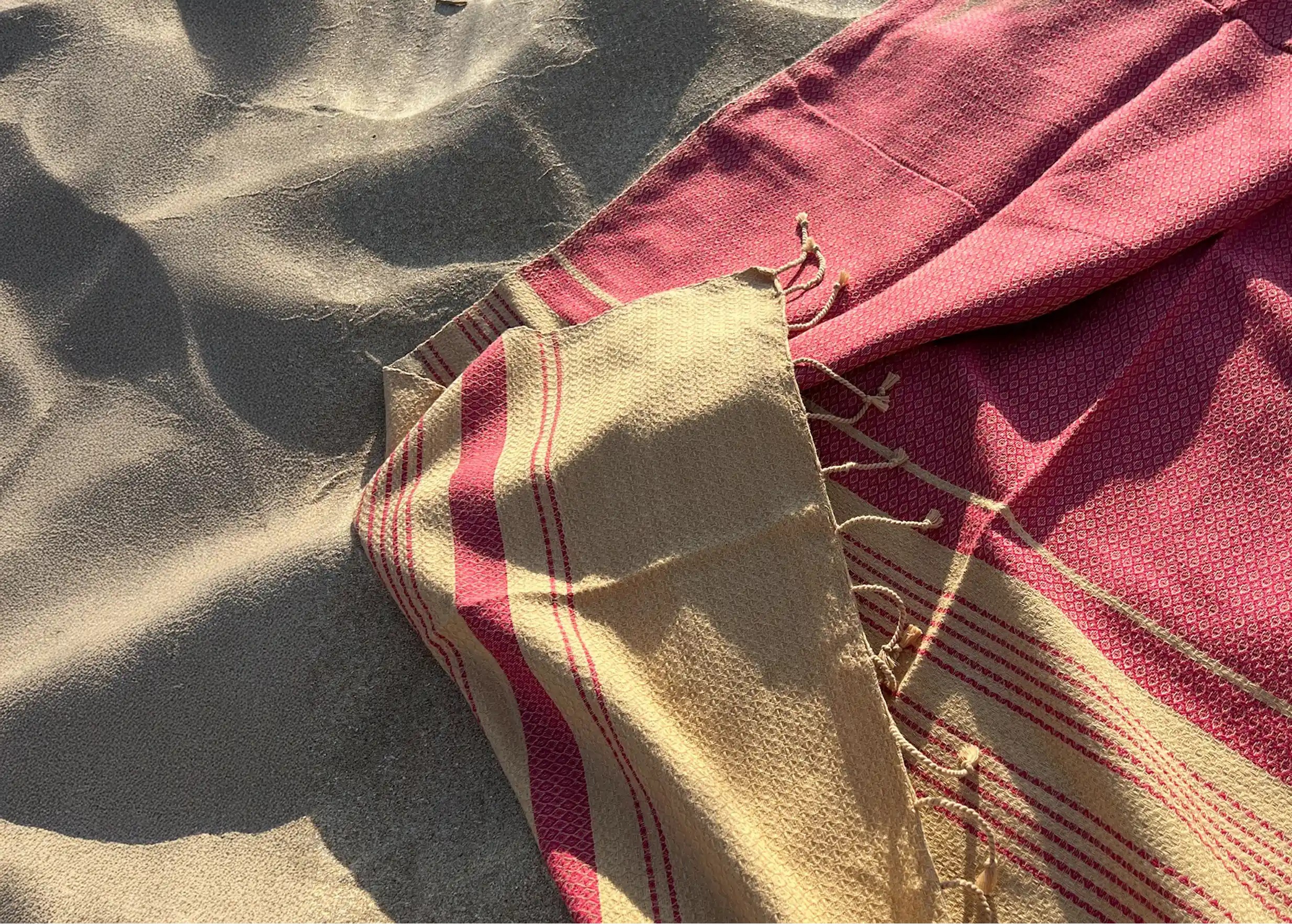 Organic cotton fouta laid out on the sand at the beach, sunlight reflecting off the fouta