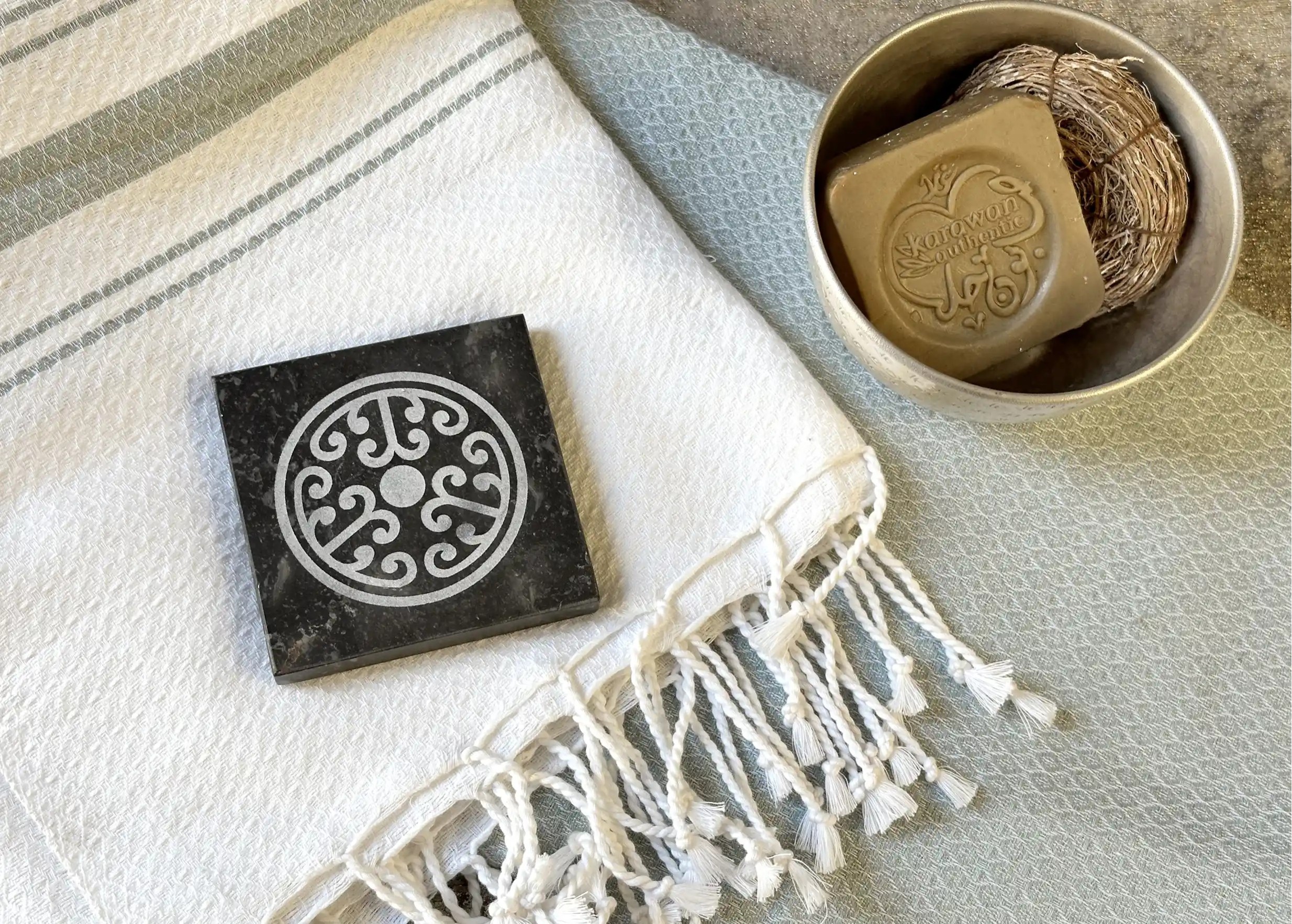 Porte-savon en marbre noir sur une fouta en coton biologique, accompagnée d’un savon d’Alep