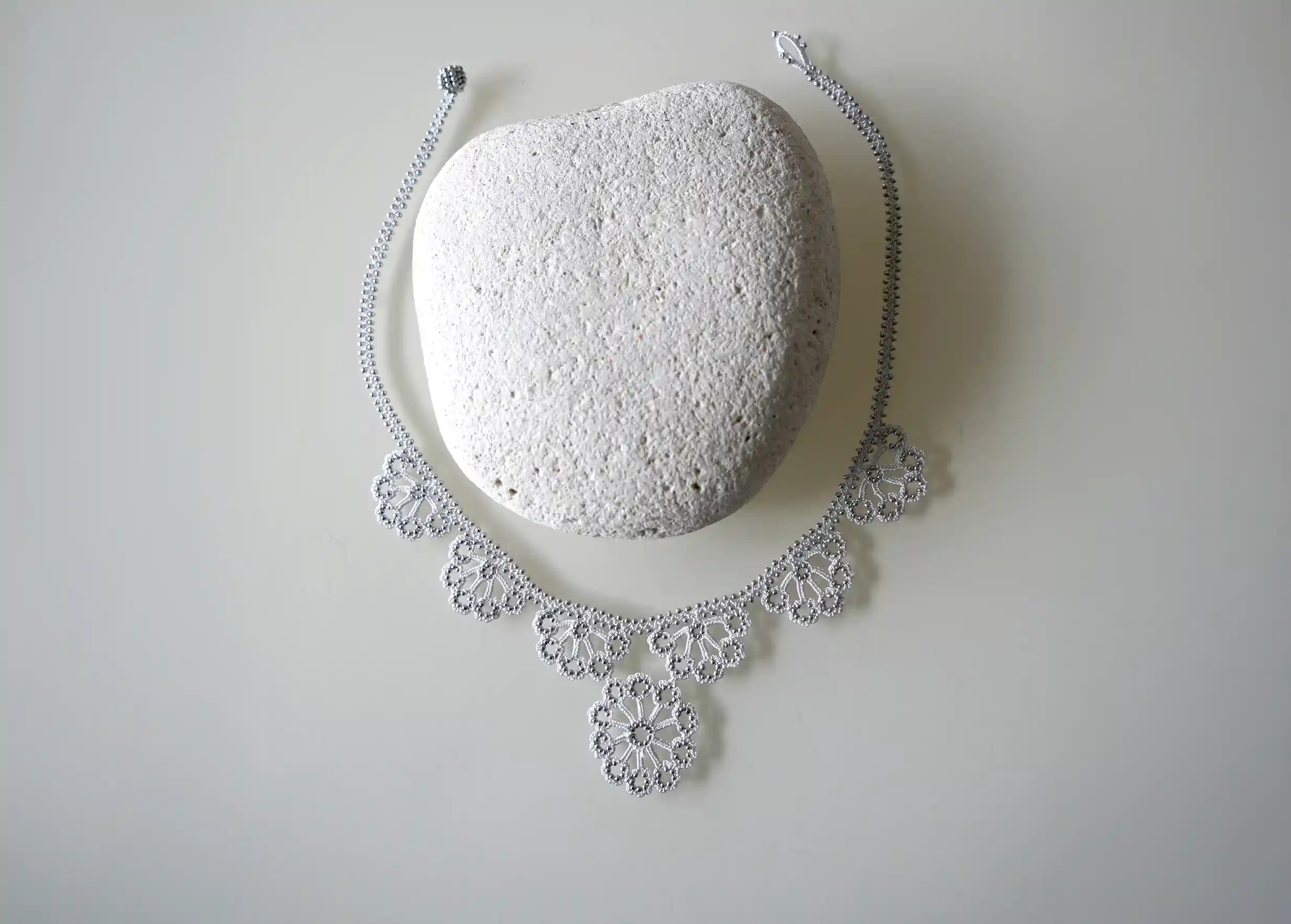 Motif floral en dentelle, orné de perles, sur un collier Hawa de couleur gris argent